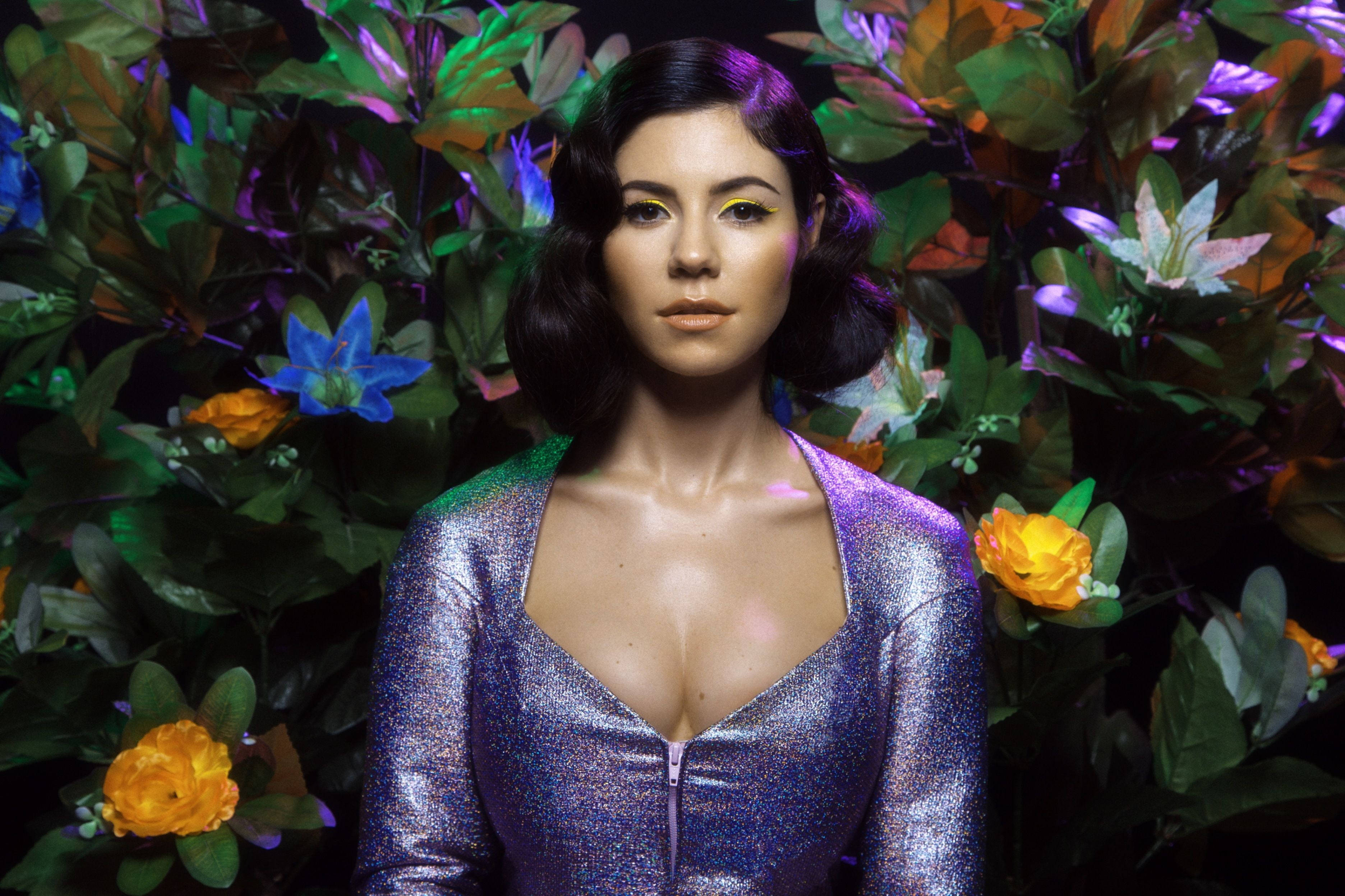 marina 桌布 壁紙 — 一位身穿閃亮紫色連衣裙的女性站在充滿活力的花卉背景前，背景以霓虹燈照亮。