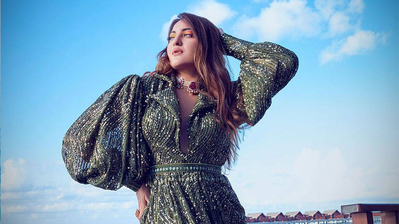 Sonakshi Sinha 桌布 壁紙 — 一位身穿閃亮綠色連衣裙的女性在藍天白雲下自信地擺姿勢。