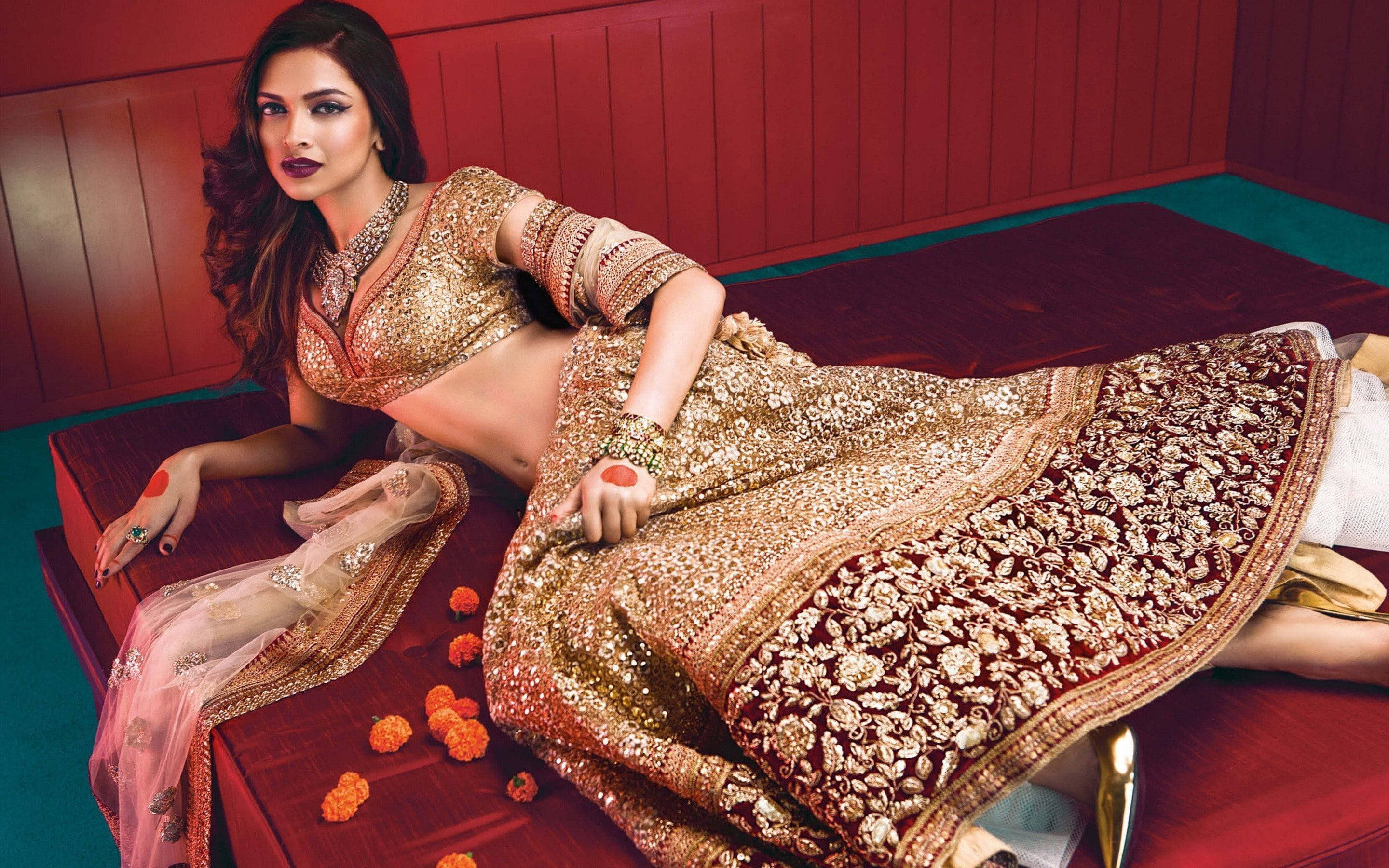 Deepika 桌布 壁紙 — 一位身穿閃亮金色和栗色長裙的女子，在萬壽菊環繞的紅色平台上斜倚著。