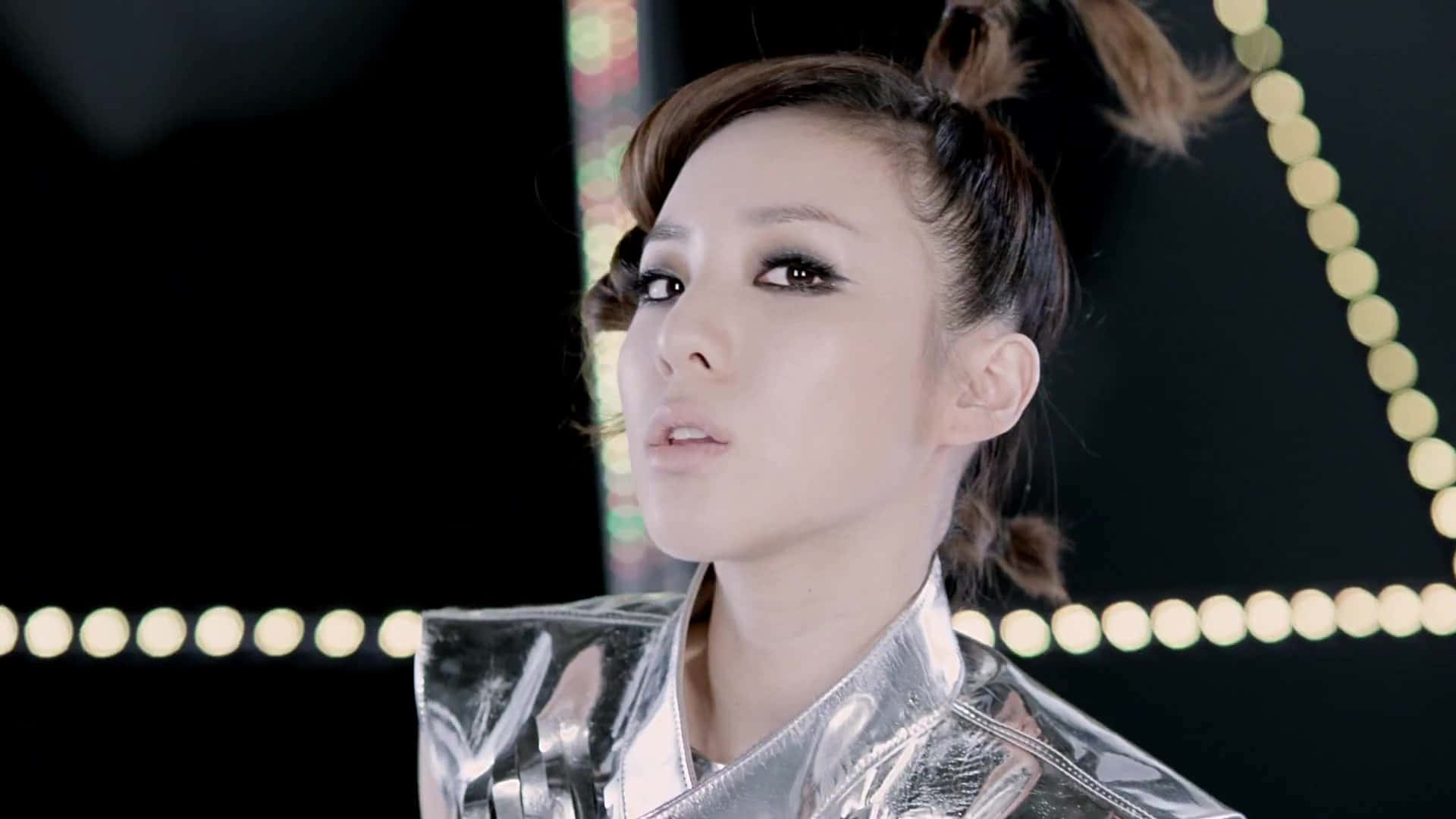 2NE1 桌布 壁紙 — 一位身穿閃亮銀色服裝的女性在黑暗背景下仰望發光的圓形燈光。