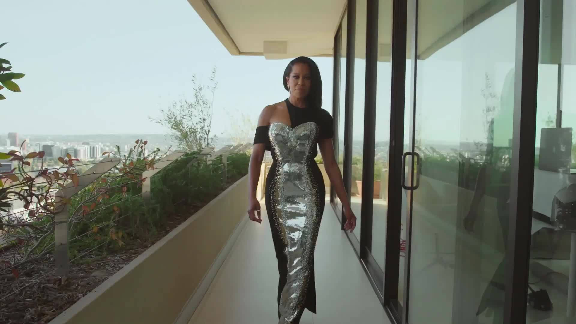 Celebrity 桌布 壁紙 — 一位身穿閃亮銀黑色連衣裙的女性自信地走在可俯瞰城市景觀的現代陽台上。