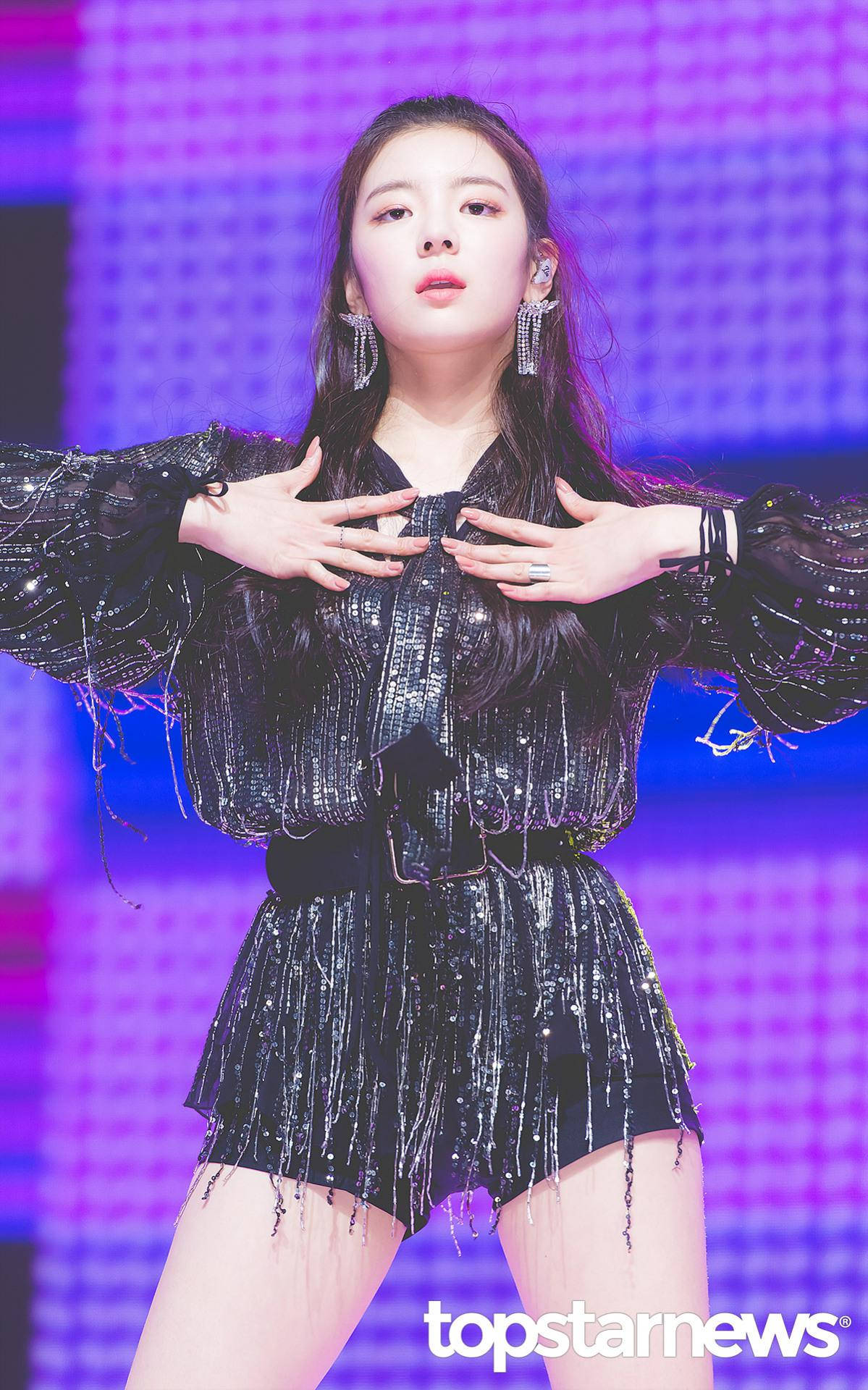 Lia 桌布 壁紙 — 一位身穿閃亮黑色服裝的女表演者在充滿活力的紫色網格舞台背景下自信地擺姿勢。