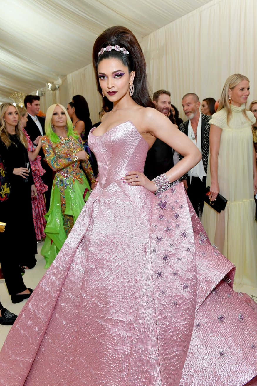 Met Gala 桌布 壁紙 — 一位身穿閃爍粉紅色禮服、飾有星星裝飾的女性，在室內華麗的晚會上自信地擺姿勢，背景有賓客。
