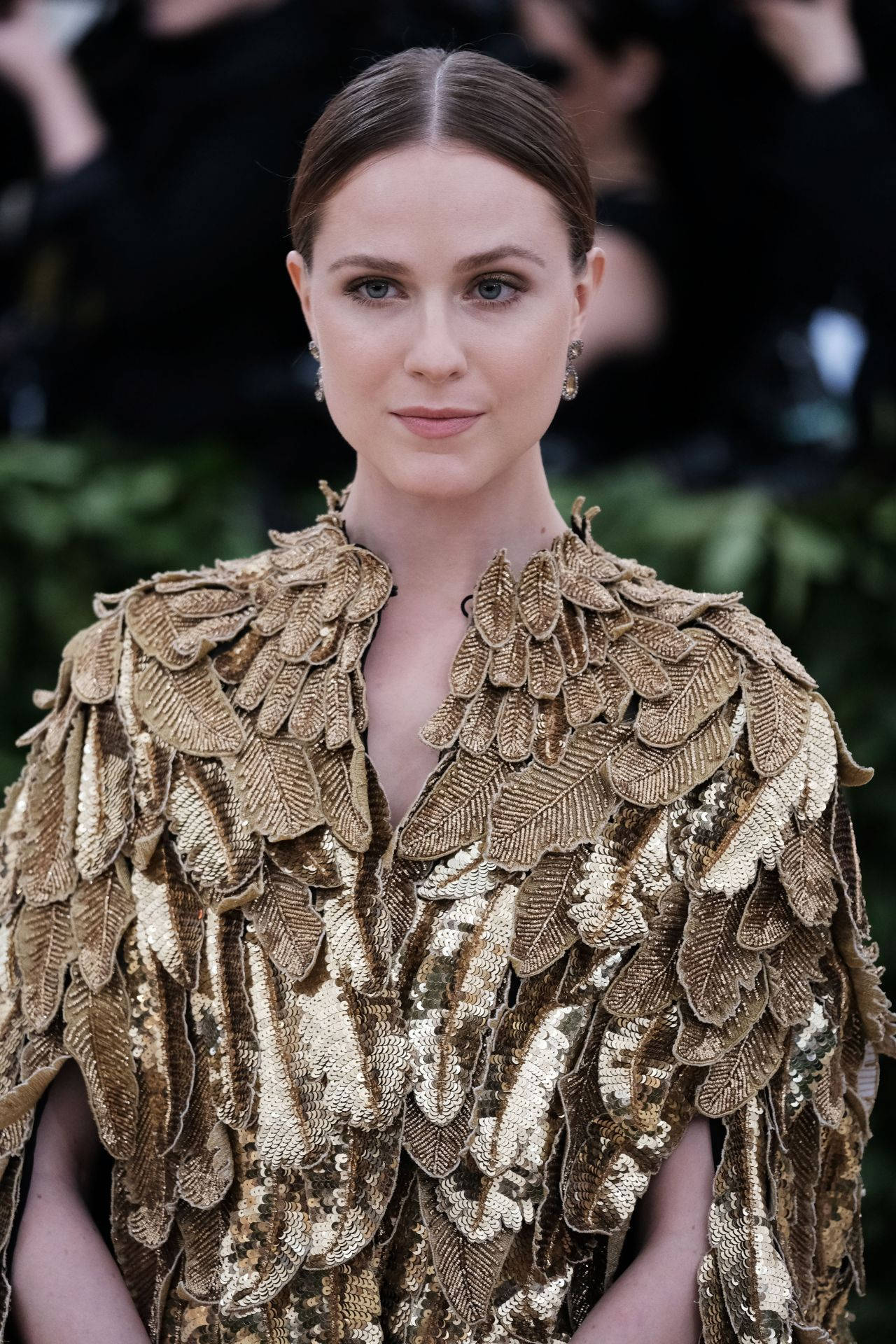 Celebrity 桌布 壁紙 — 一位身穿閃爍金色葉片裝飾長裙的女性，在模糊的綠色背景下以平靜的表情擺姿勢。
