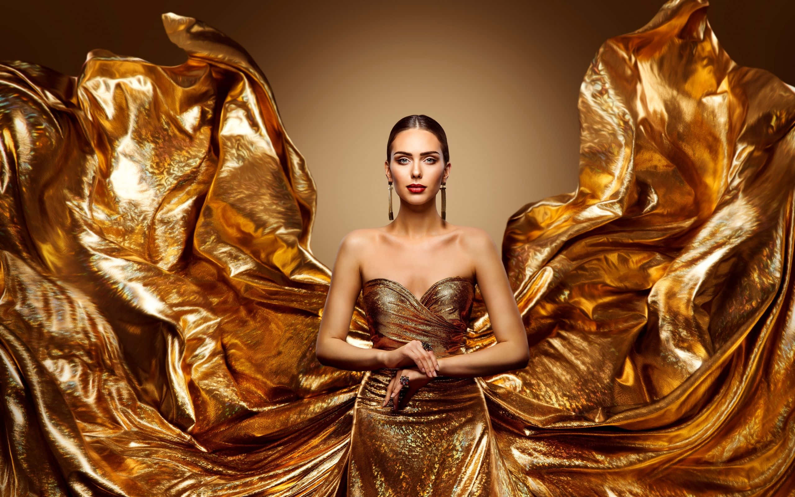 Met Gala 桌布 壁紙 — 一位身穿閃爍金色長裙的優雅女士，在溫暖的棕色背景下，被流動的金屬布料環繞著。