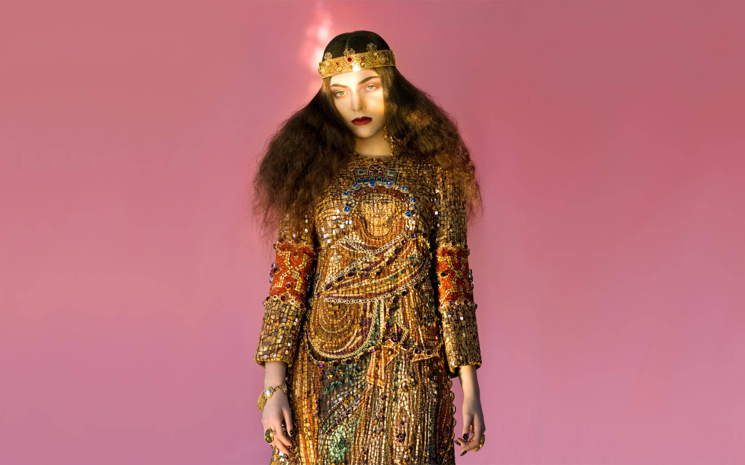 蘿兒 桌布 壁紙 — 一位身穿閃閃發光金色珠寶禮服和皇冠的女性，站在柔和的粉紅色工作室背景前，燈光效果戲劇化。