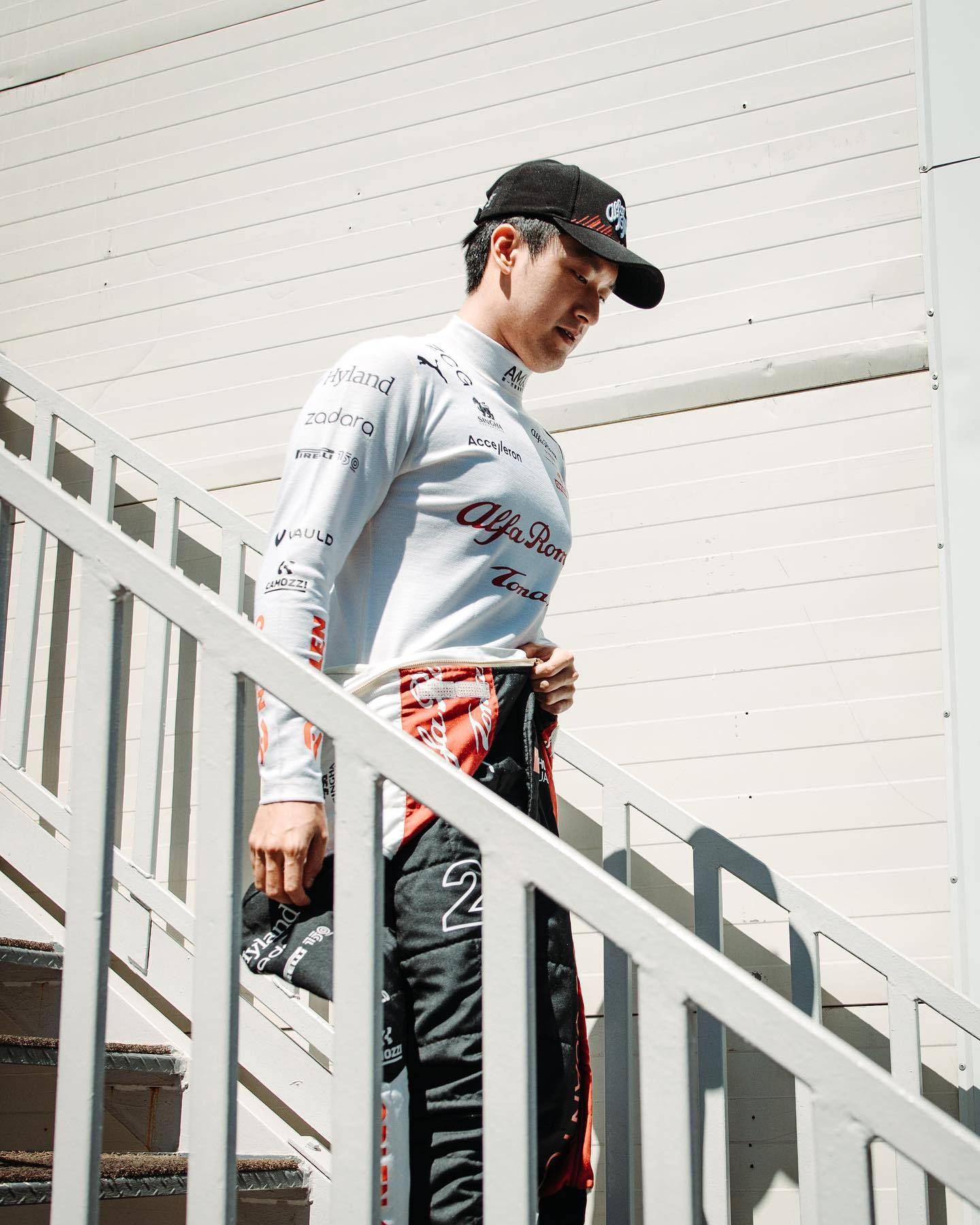 Racing 桌布 壁紙 — 一位身穿阿爾法羅密歐裝備的賽車手站在白色樓梯上，在明亮的陽光下調整褲子。
