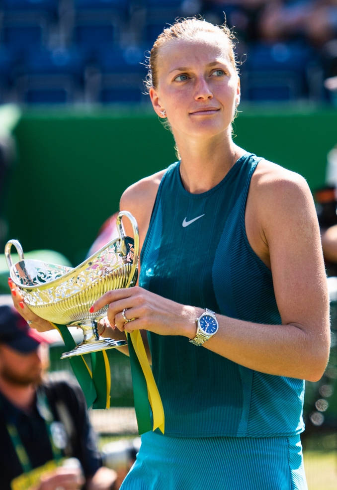 Trophy 桌布 壁紙 — 一位身穿青綠色Nike服裝的女網球運動員在明亮的日光下，手持一個閃閃發光的金色獎盃，上面繫著綠色和黃色的絲帶。