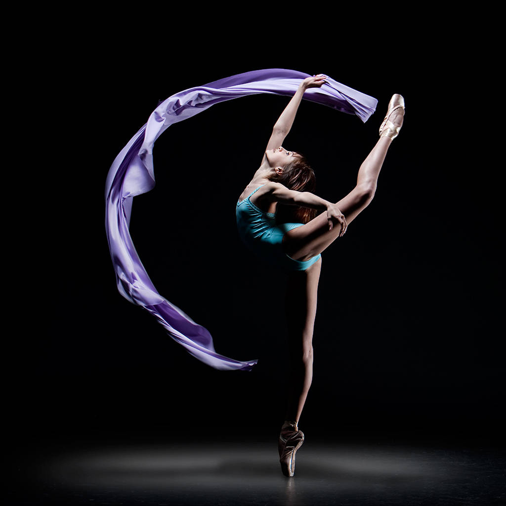 ballerina 桌布 壁紙 — 一位身穿青綠色緊身衣的芭蕾舞者，在純黑背景下優雅地踮起腳尖，同時揮舞著一條飄逸的紫色絲帶。