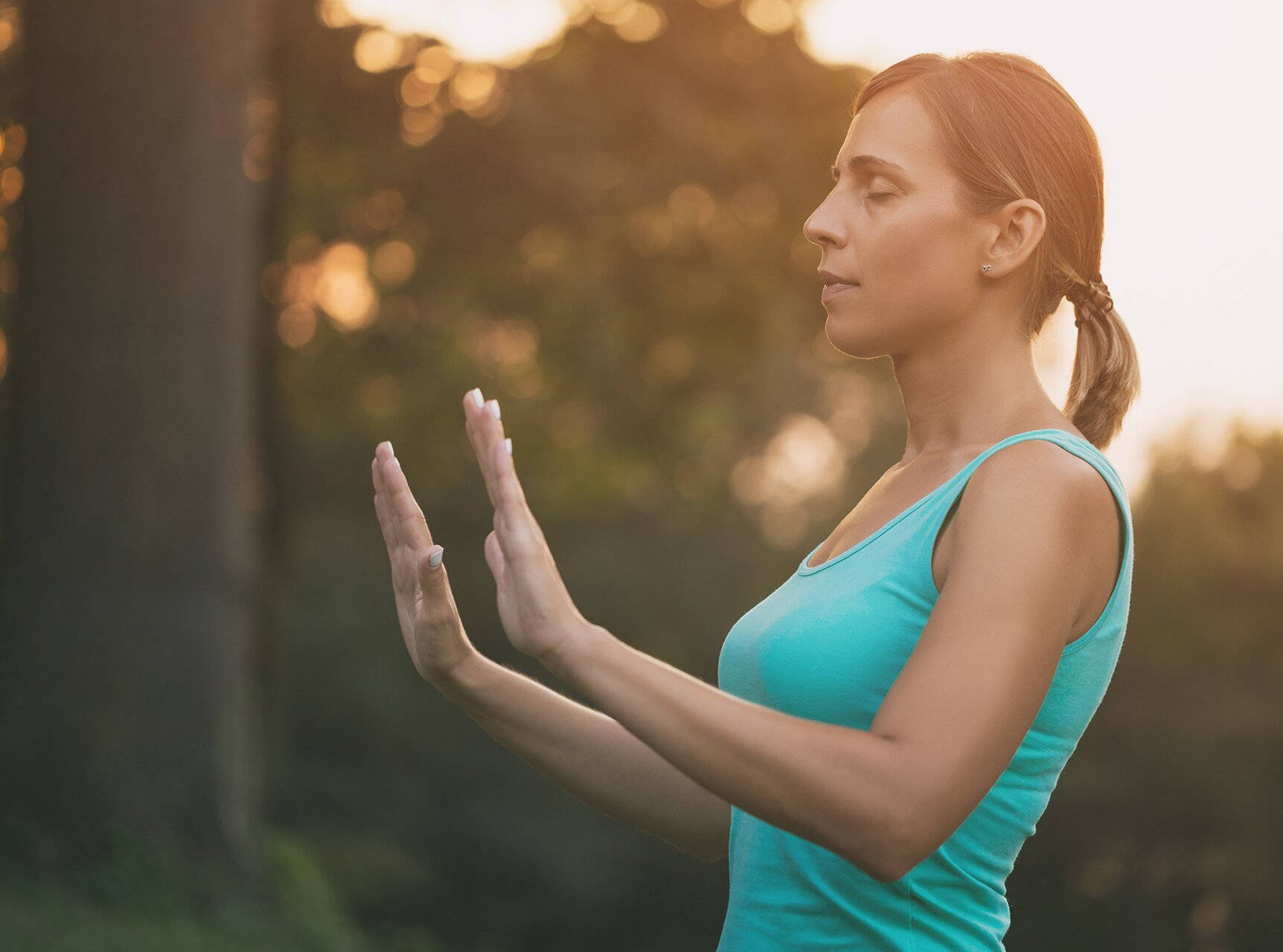 Exercise 桌布 壁紙 — 一位身穿青綠色背心的女性在陽光明媚的森林中平靜地冥想，背景是金色的散景效果。