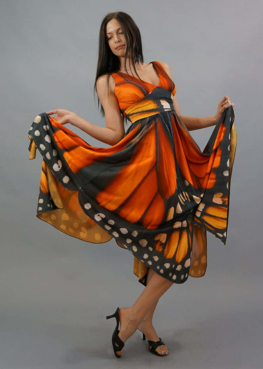 Butterfly Wing Dress 桌布 壁紙 — 一位身穿飄逸帝王蝶印花連衣裙的女性在純灰色工作室背景前優雅地擺姿勢。