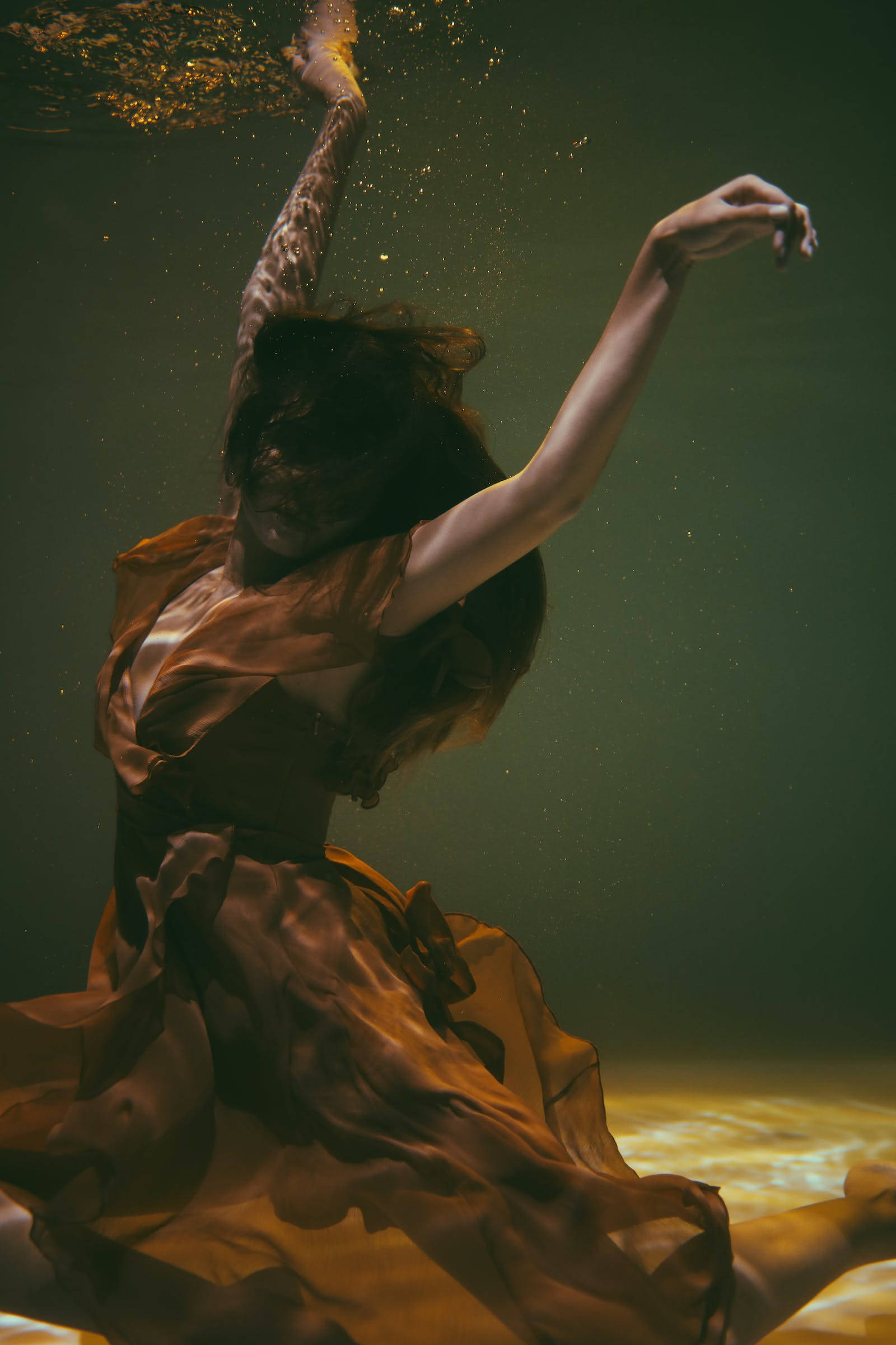 Aesthetic Photography 桌布 壁紙 — 一位身穿飄逸棕色連衣裙的女性在水中優雅地跳舞，金色的光線從上方灑下。