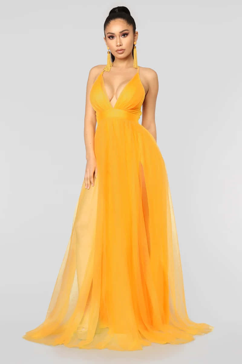 Yellow Fashion 桌布 壁紙 — 一位身穿飄逸橙色長裙、高開衩和相配耳環的女性在純白色背景前擺姿勢。
