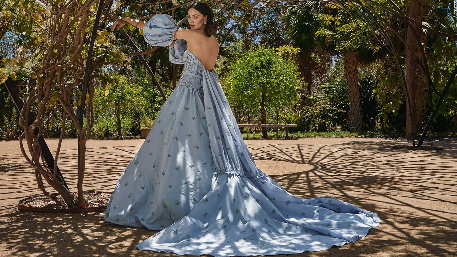 Bride's Dress 桌布 壁紙 — 一位身穿飄逸淺藍色刺繡花卉長裙的女性，在茂密花園的斑駁陽光下優雅地擺姿勢。
