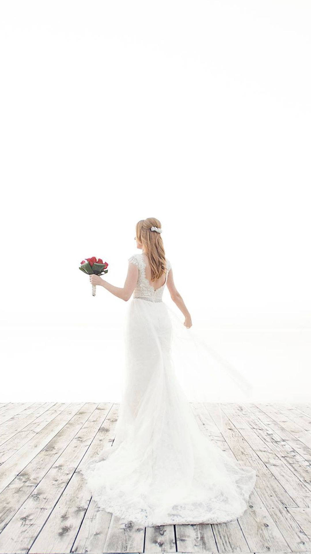 Bridal 桌布 壁紙 — 一位身穿飄逸白色婚紗的新娘，在一個風化的木甲板上，手持一束紅玫瑰，背對著明亮的白色背景走開。
