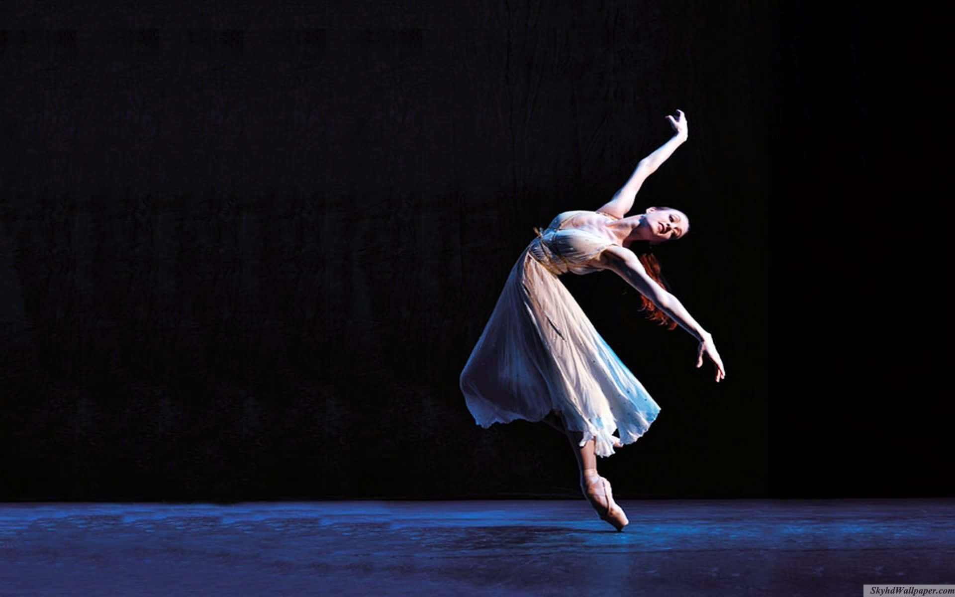 Ballet 桌布 壁紙 — 一位身穿飄逸白色連衣裙的芭蕾舞者在深色背景下，於戲劇性的藍色舞台燈光下優雅地踮起腳尖跳躍。