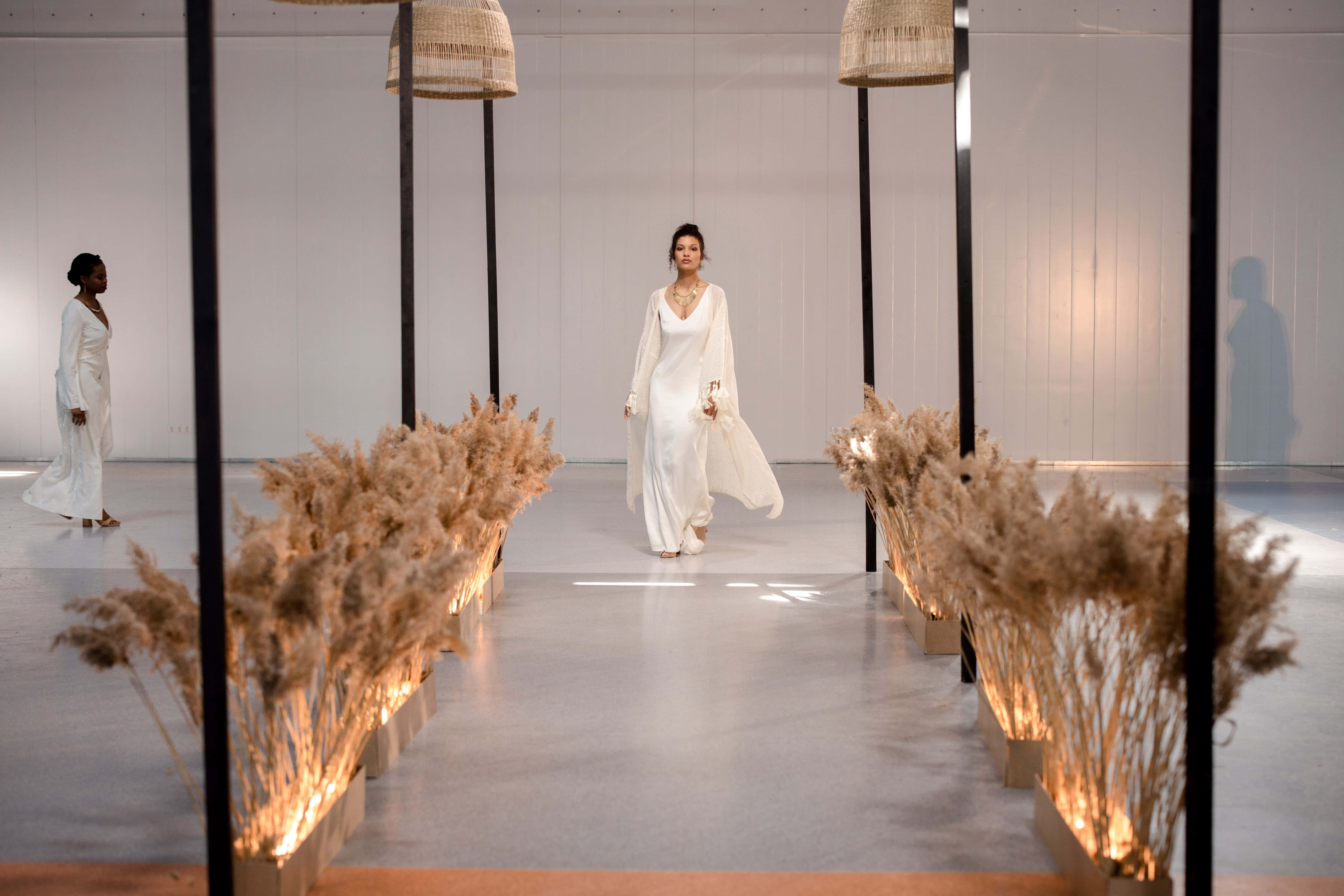 Runway 桌布 壁紙 — 一位身穿飄逸白色長裙的女性，在兩旁佈滿發光蒲葦裝飾的簡約伸展台上行走。