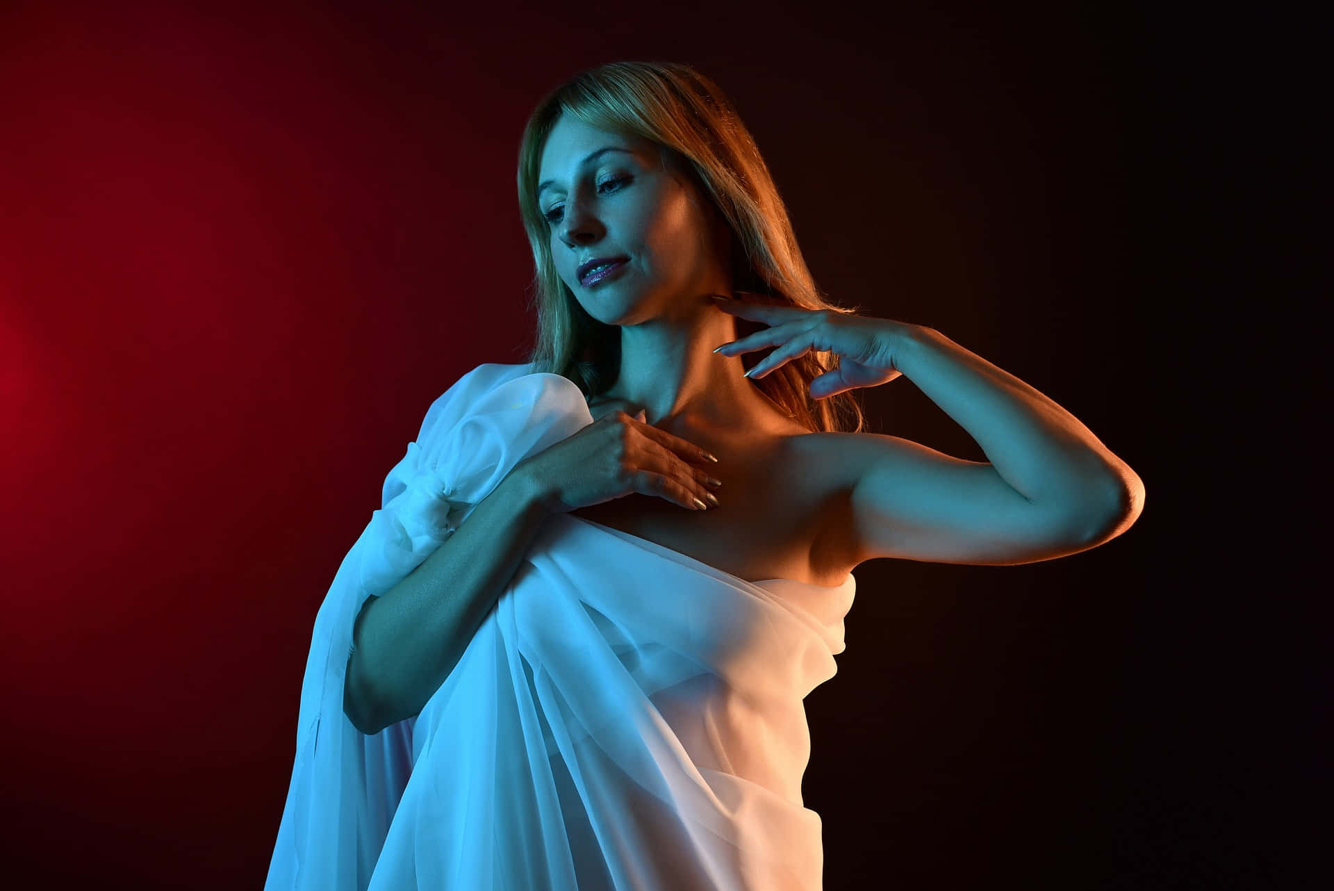Photoshoot 桌布 壁紙 — 一位身穿飄逸白色長裙的女性，在色彩繽紛的攝影棚燈光下，於戲劇性的紅黑背景前優雅地擺姿勢。
