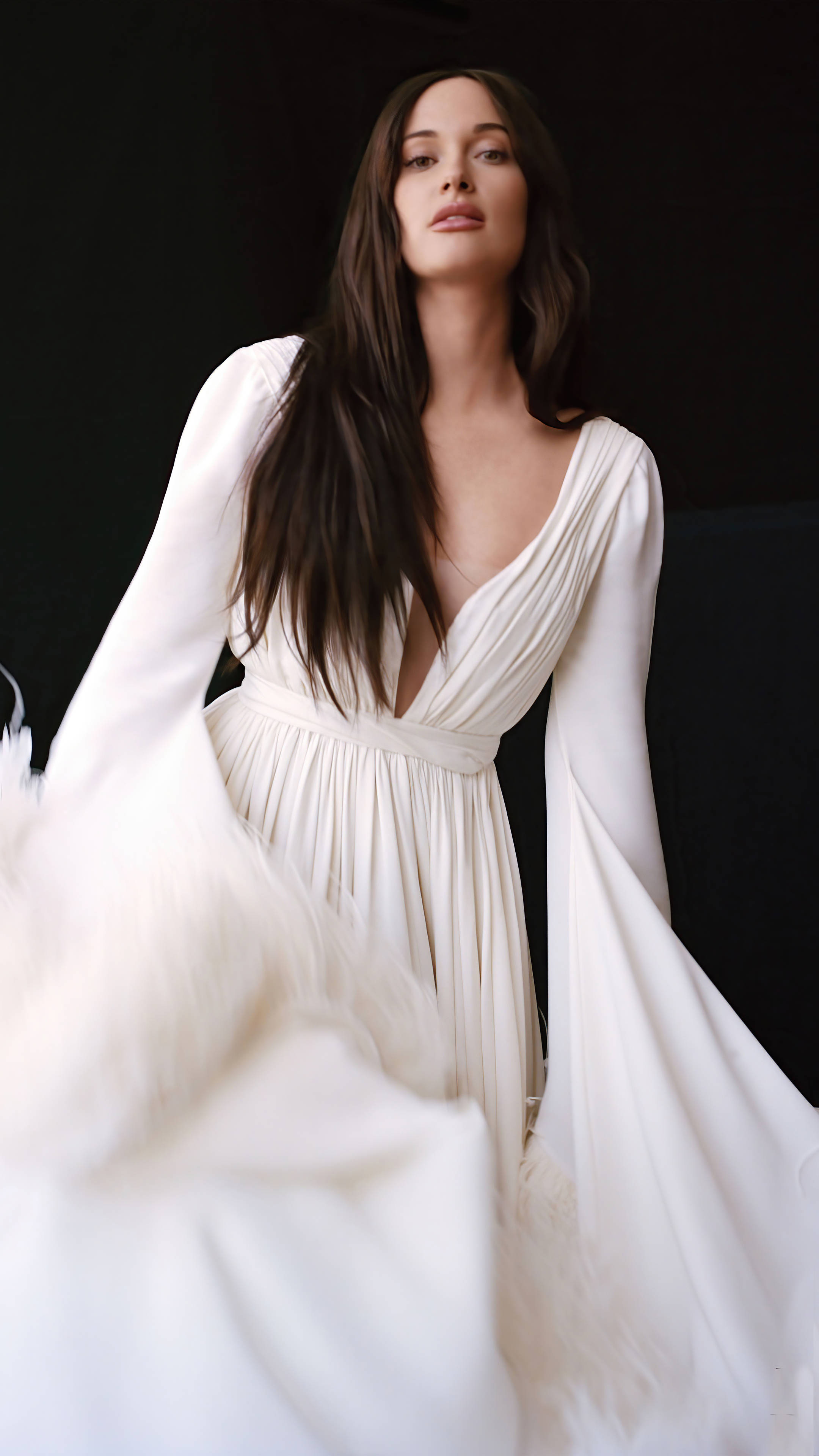 Kacey Musgraves 桌布 壁紙 — 一位身穿飄逸白色長裙的女性站在純黑背景前，長長的深色頭髮如瀑布般垂下，布料在她周圍旋轉。