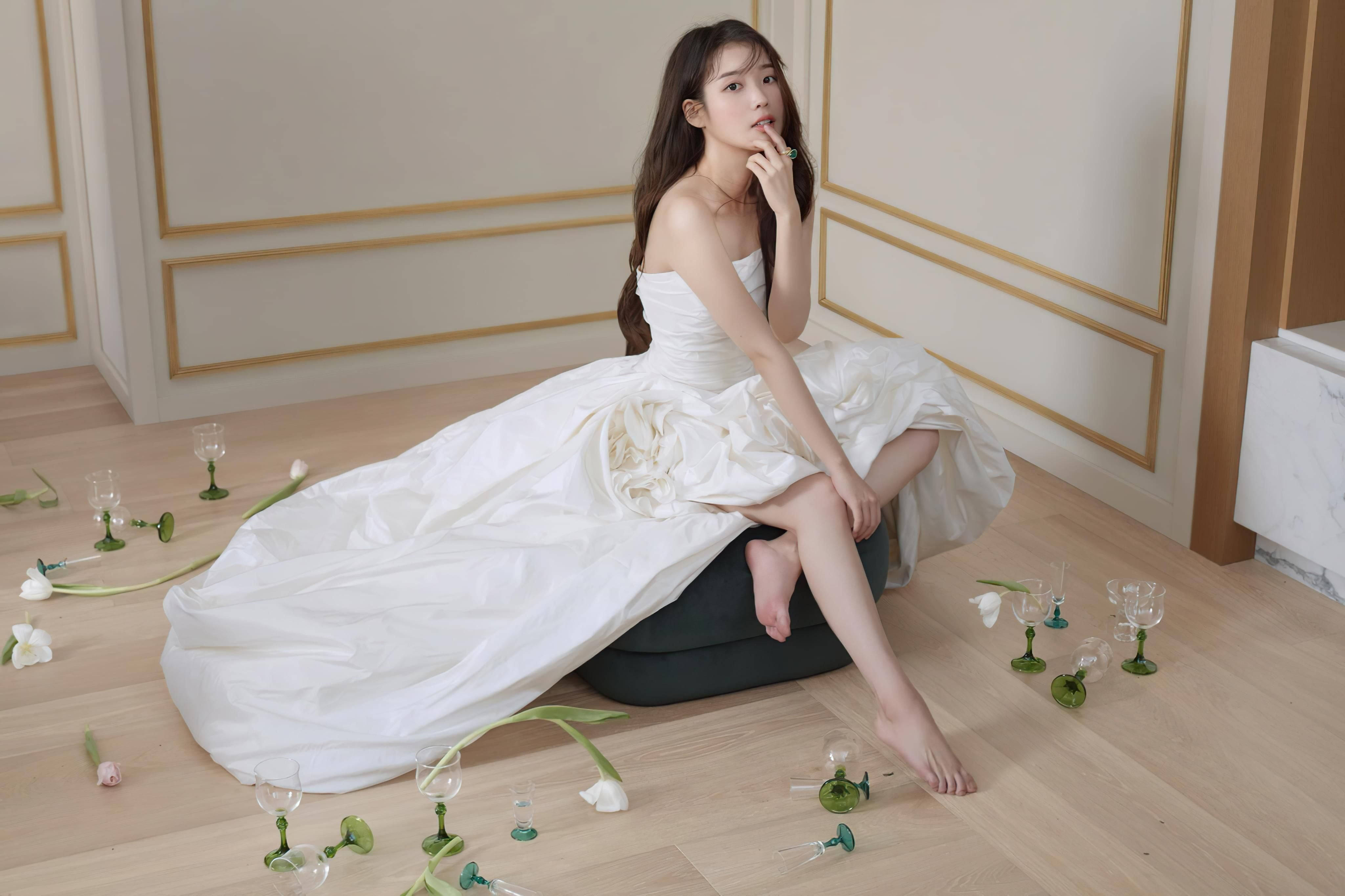 女孩 桌布 壁紙 — 一位身穿飄逸白色長裙的女性赤腳坐在黑色坐墊上，周圍散落著酒杯和白色鬱金香，地板為木質。