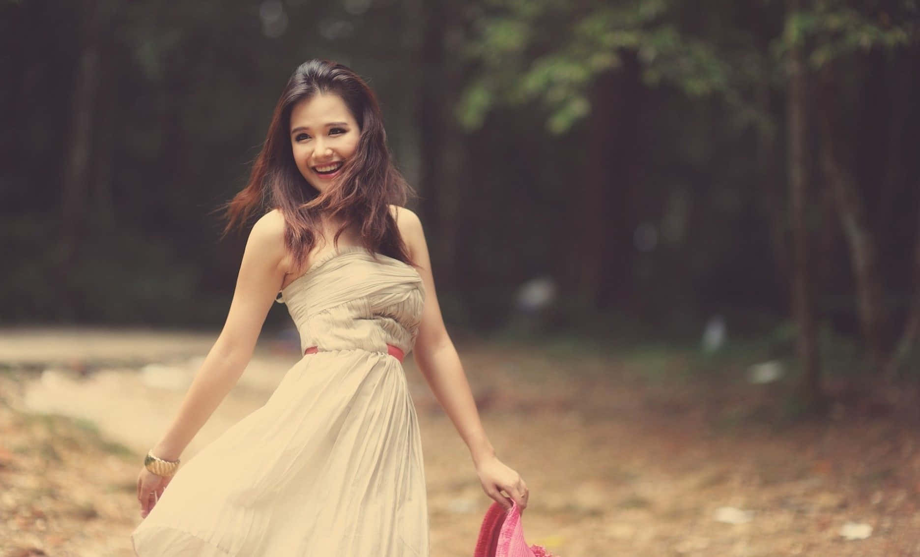 Woman 桌布 壁紙 — 一位身穿飄逸米色連衣裙的快樂女人，在陽光斑駁的森林小徑上走著，笑著。