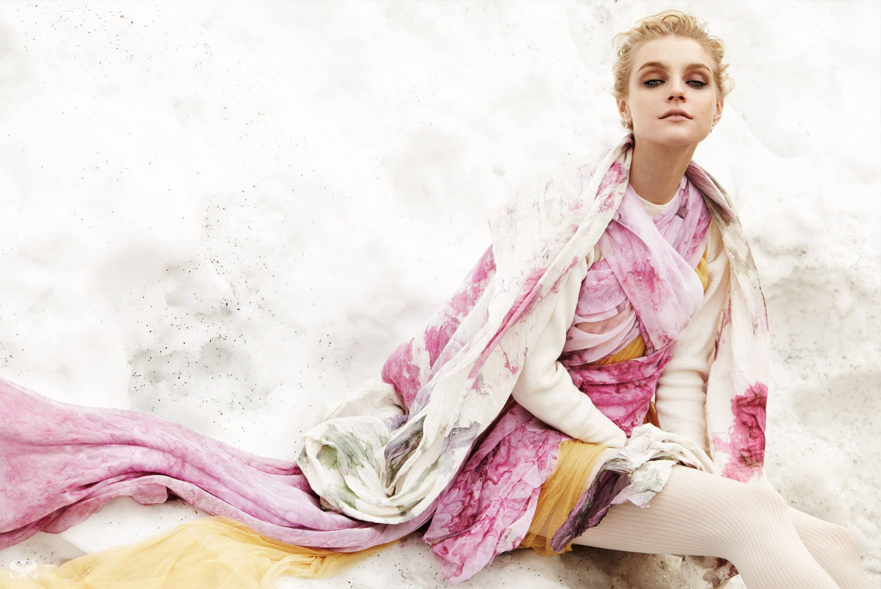 jessica stam 桌布 壁紙 — 一位身穿飄逸粉紅和黃色服飾的女性，在柔和的燈光下，優雅地坐在有紋理的白色背景前。
