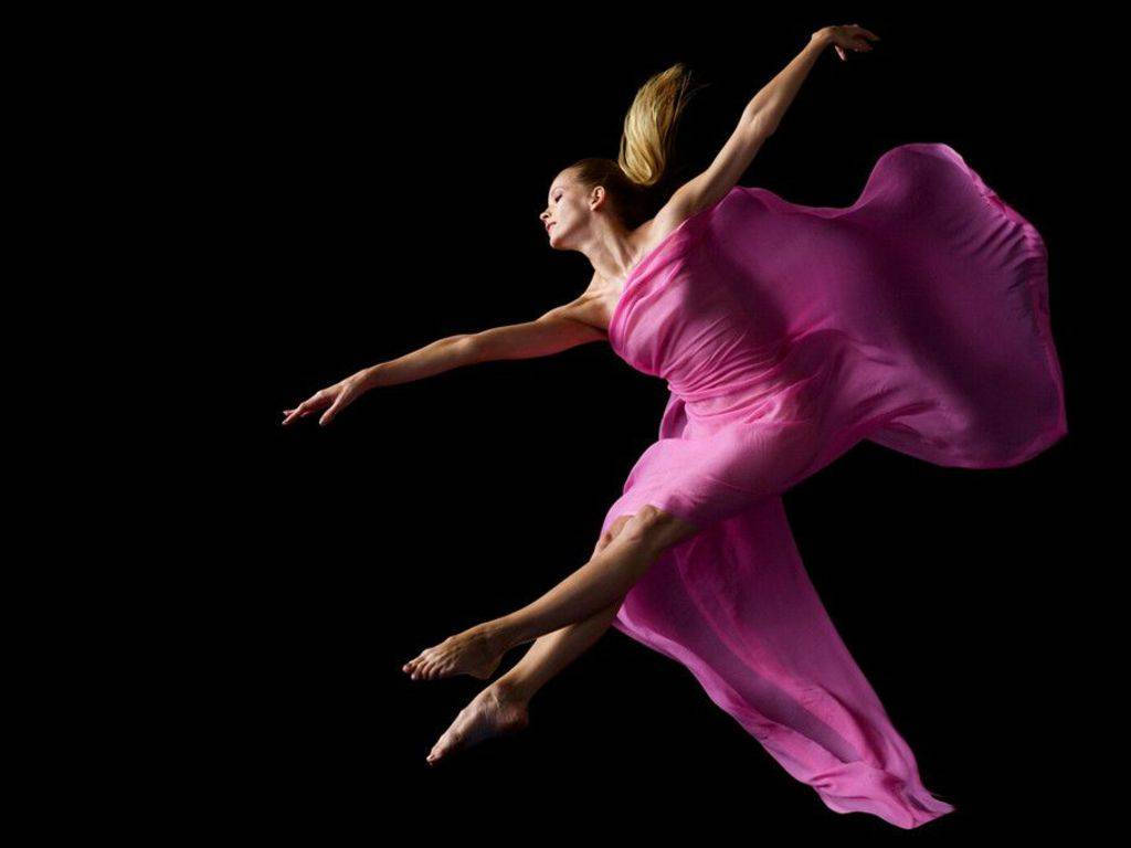 Ballet 桌布 壁紙 — 一位身穿飄逸粉紅色長裙的優雅舞者，在純黑色背景前伸展雙臂凌空躍起。