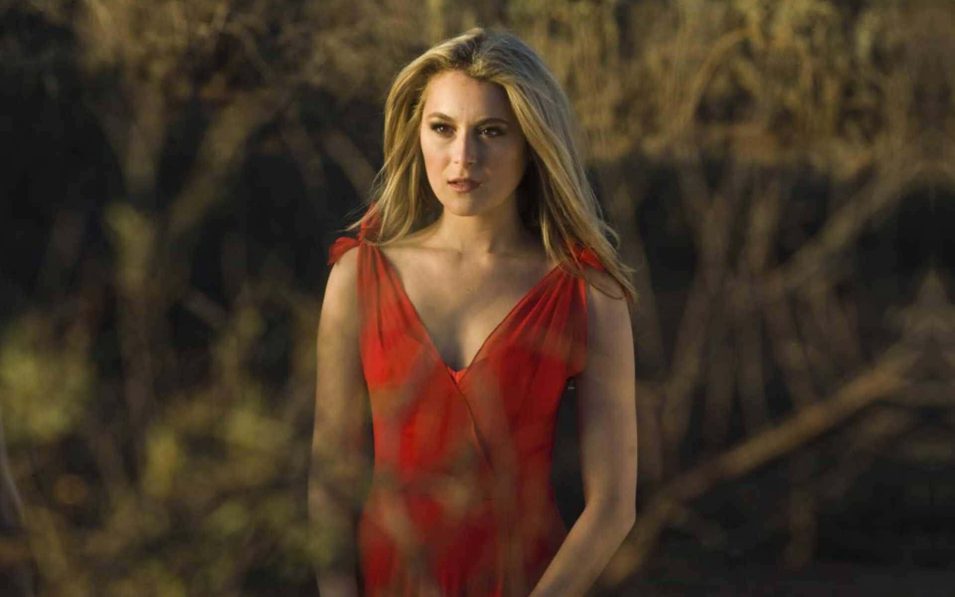 Alexa Penavega 桌布 壁紙 — 一位身穿飄逸紅裙的女子站在金棕色的灌木叢中，柔和陽光照亮她的金髮。