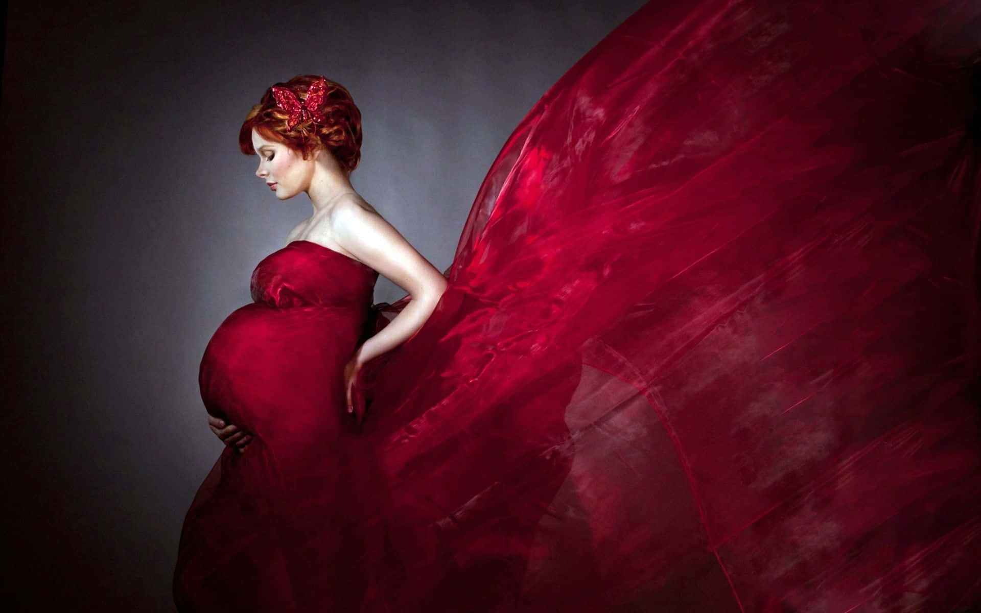 Pregnant 桌布 壁紙 — 一位身穿飄逸紅裙的孕婦優雅地站在深色背景前，手放在肚子上，布料戲劇性地飄揚。