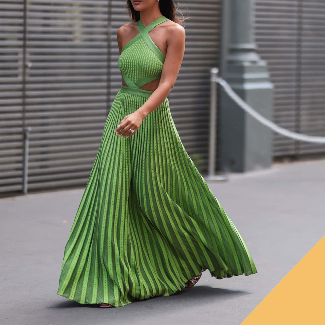 Long Dress 桌布 壁紙 — 一位身穿飄逸綠色百褶長裙的女性自信地走在城市街道上，身後是金屬百葉窗。