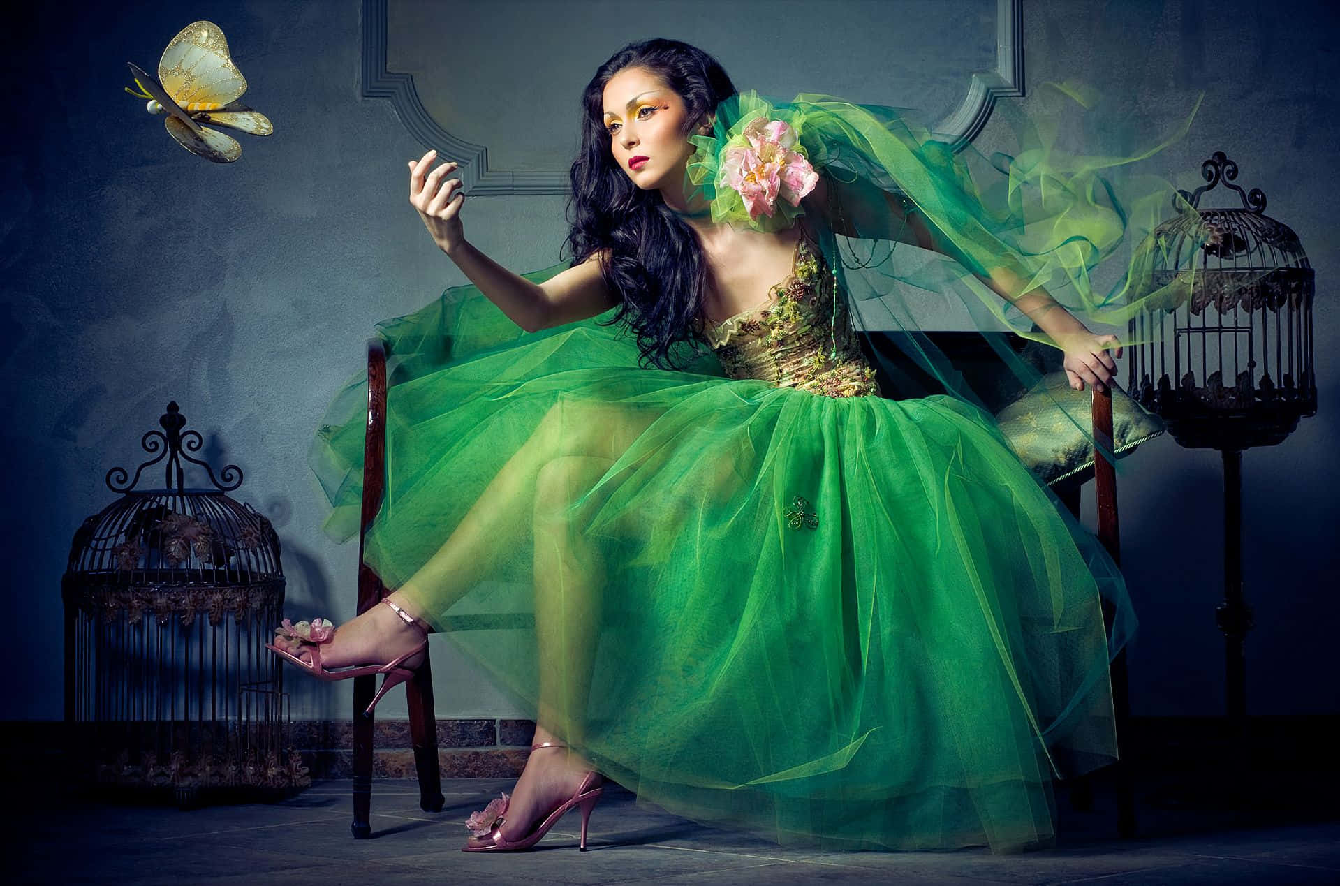 Butterfly Dress 桌布 壁紙 — 一位身穿飄逸綠色長袍的女性優雅地坐在裝飾華麗的鳥籠旁的椅子上，一隻蝴蝶在附近盤旋。