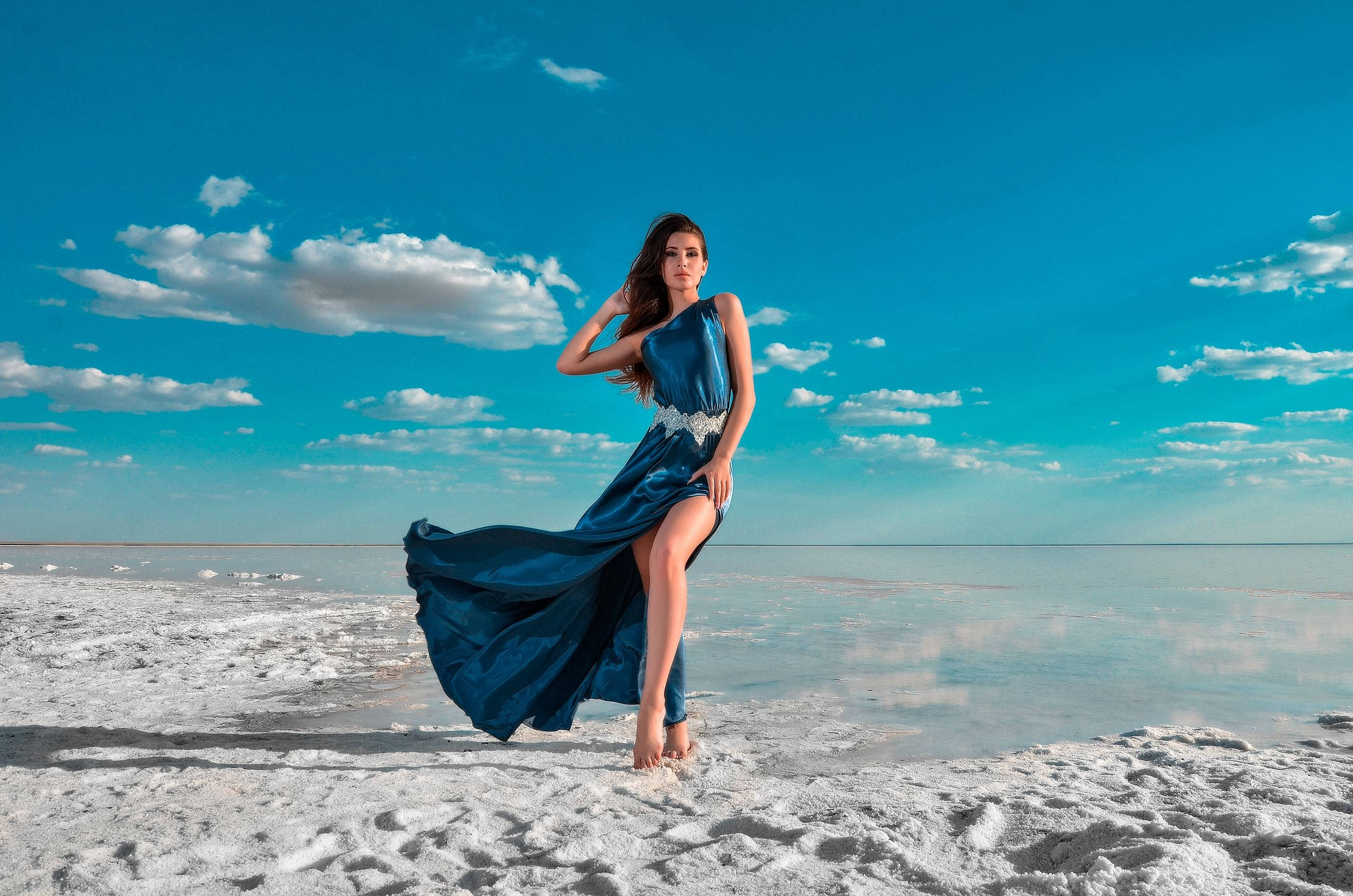 Woman Beautiful 桌布 壁紙 — 一位身穿飄逸藍色連衣裙的女子赤腳站在鹽灘上，頭頂是湛藍的天空，點綴著幾朵白雲。