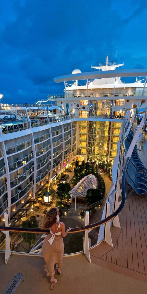Cruise 桌布 壁紙 — 一位身穿飄逸連衣裙的女性在黃昏時凝視著一艘大型郵輪的燈火通明中庭。