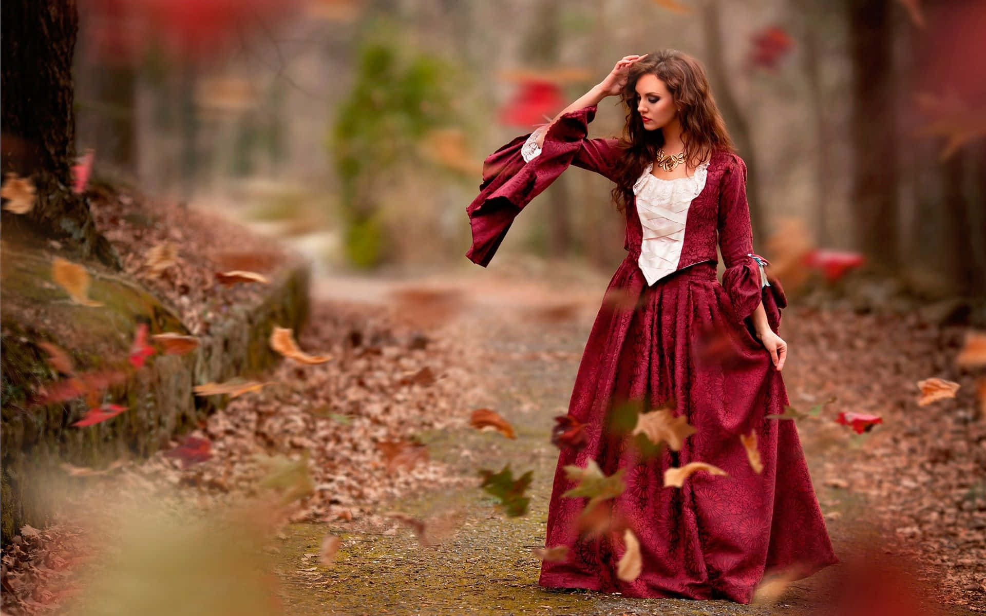 Autumn Wind 桌布 壁紙 — 一位身穿飄逸酒紅色長裙的女性走過森林，秋葉在她周圍旋轉。