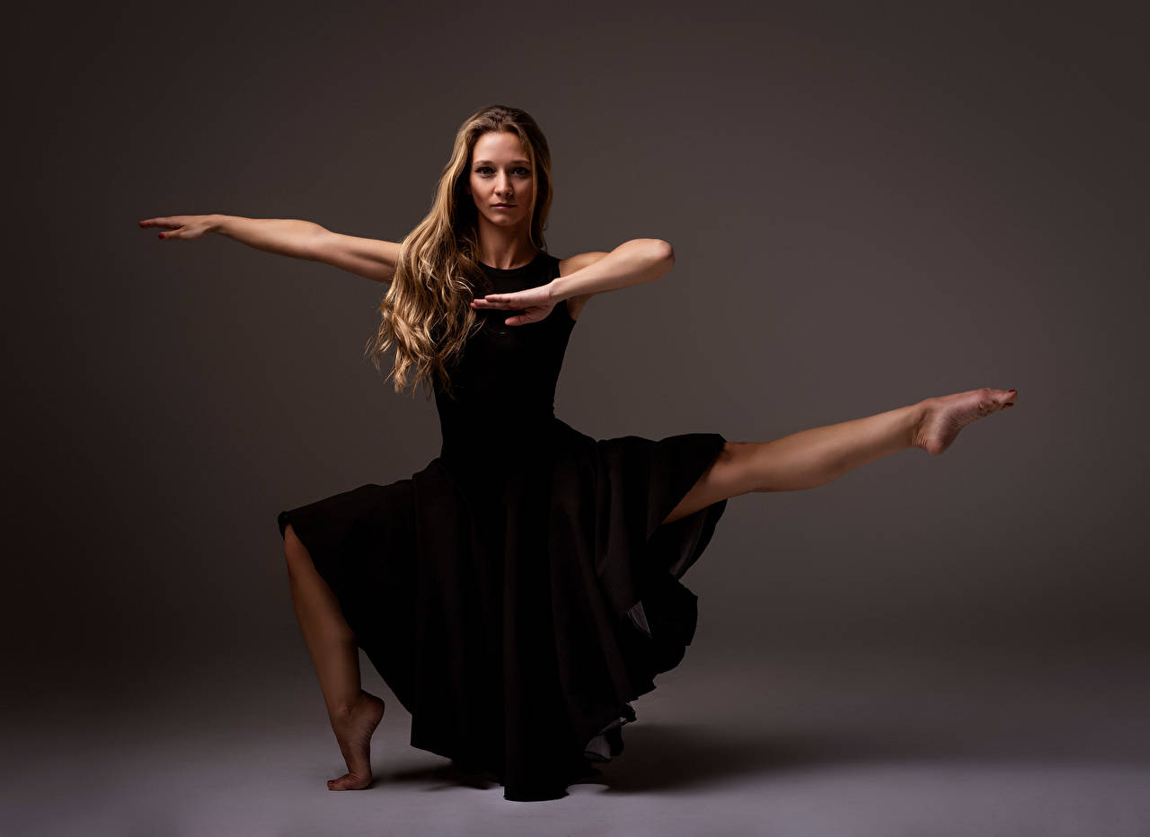 dancer 桌布 壁紙 — 一位身穿飄逸黑色連衣裙的舞者在柔和的灰色工作室背景下擺出優雅的姿勢。