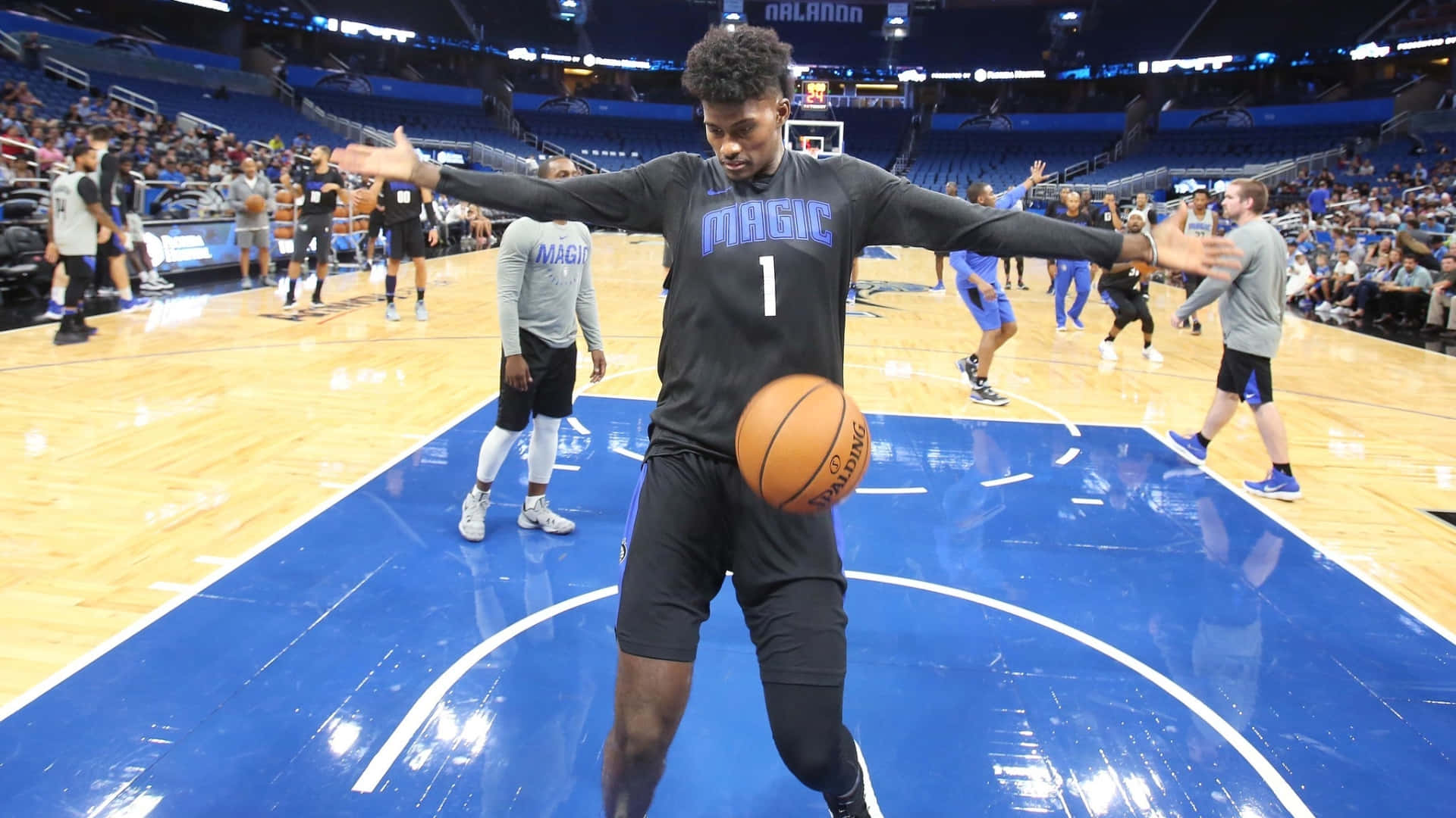 NBA 桌布 壁紙 — 一位身穿魔術隊球衣的籃球運動員在藍色球場上張開雙臂，同時將球平衡在膝蓋上。