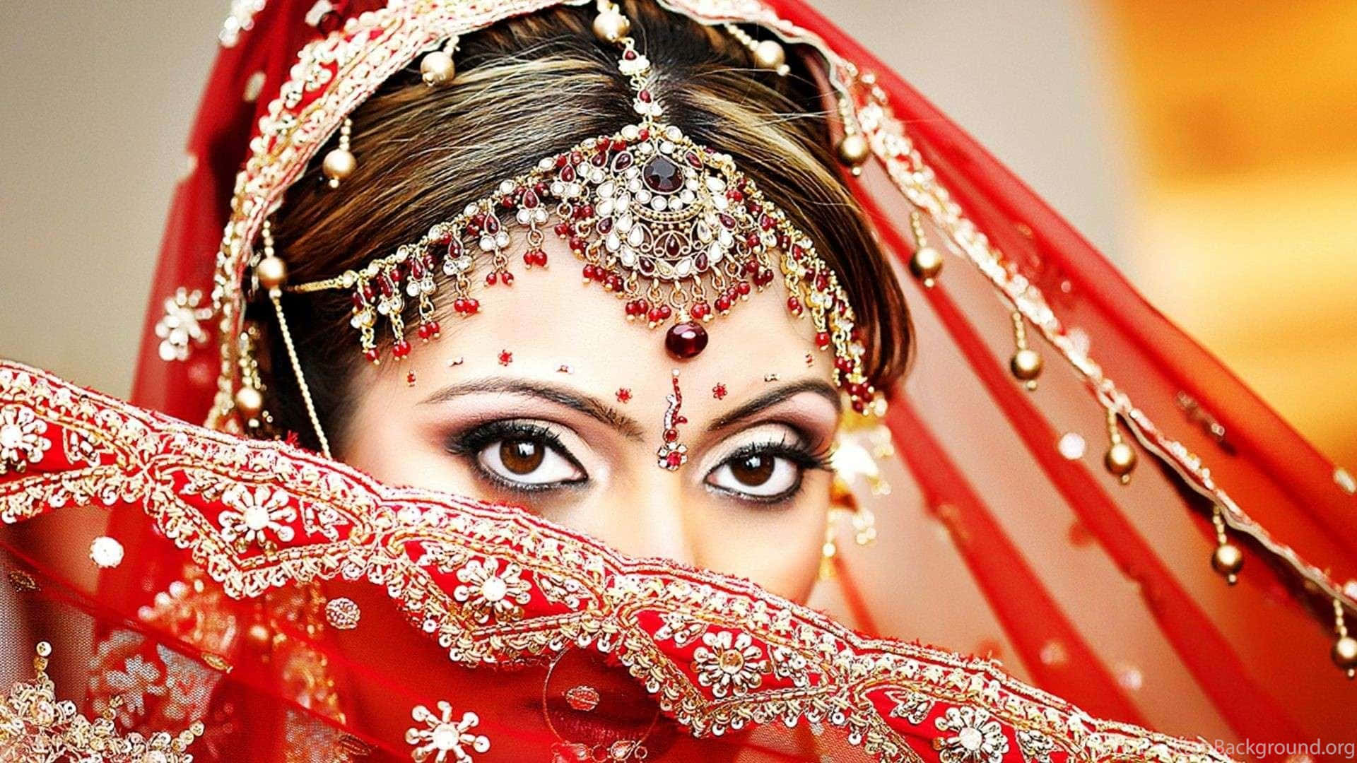 Bride 桌布 壁紙 — 一位身穿鮮紅色傳統服飾、戴著精緻金飾、面紗下目光凝視觀眾的新娘。