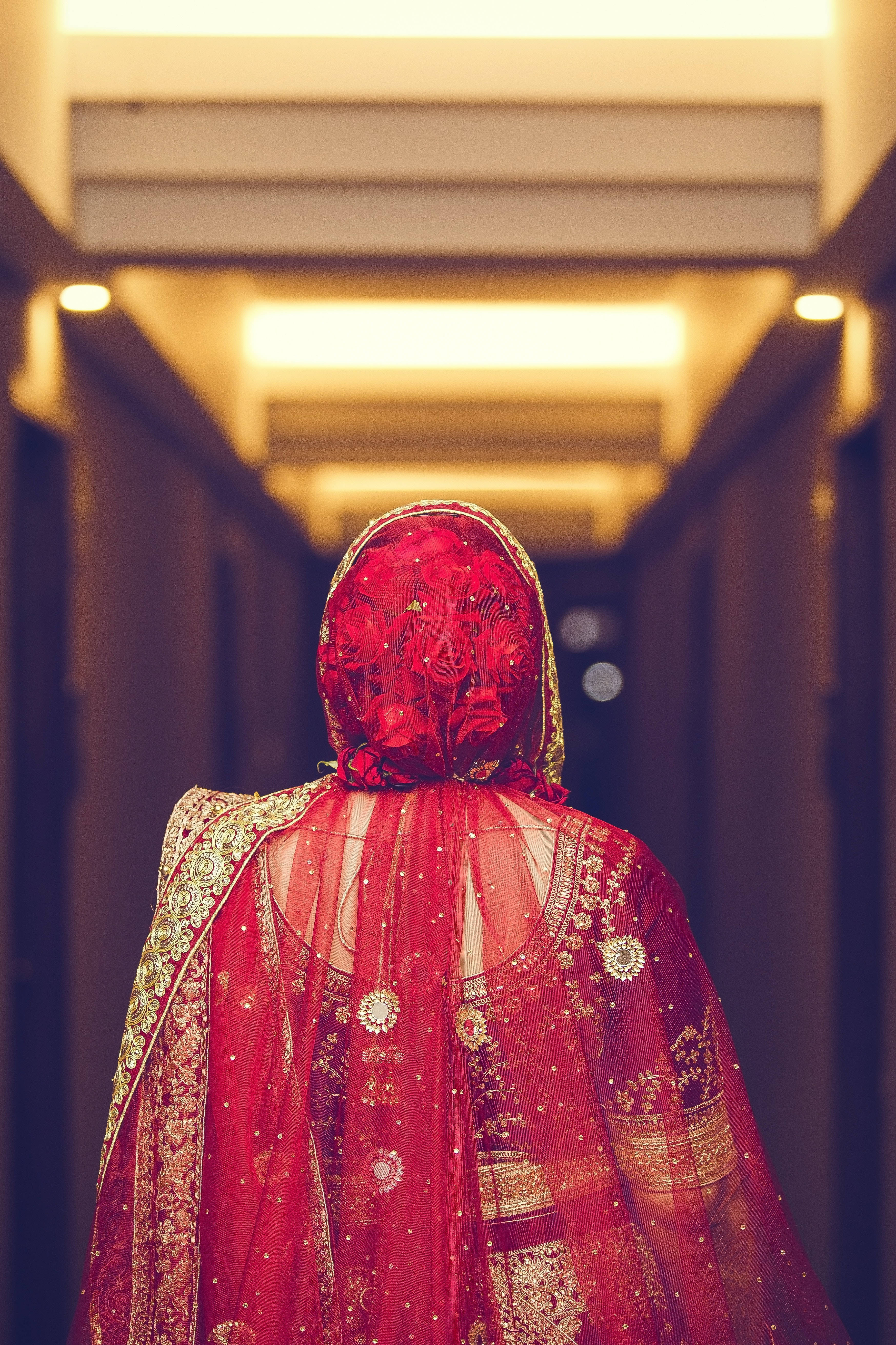 Bridal 桌布 壁紙 — 一位身穿鮮紅色刺繡 lehenga 的新娘背對鏡頭，走在燈光溫暖的飯店走廊上。