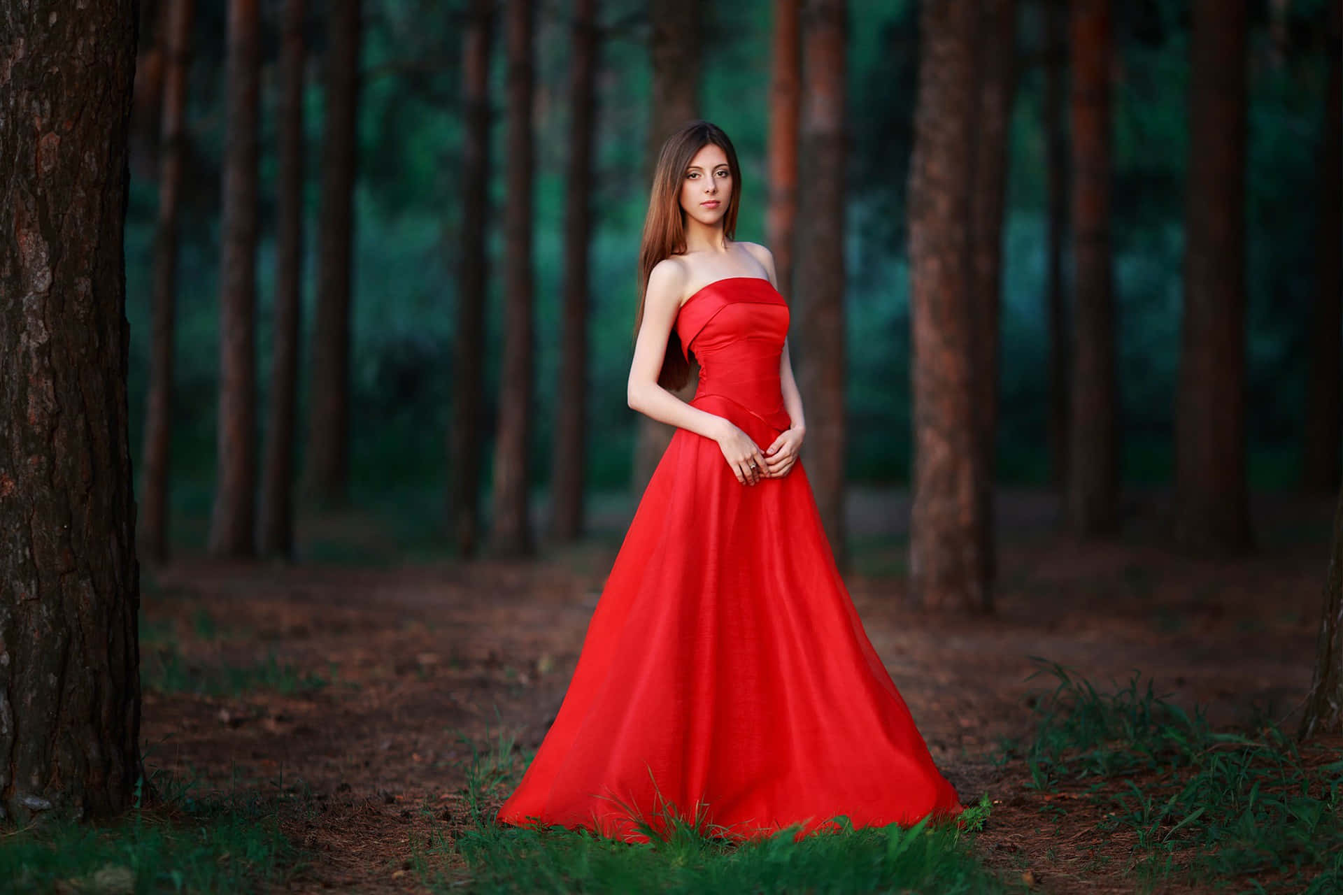 Woman 桌布 壁紙 — 一位身穿鮮紅色無肩帶禮服的女士，在寧靜的森林中優雅地站在高大的松樹之間。