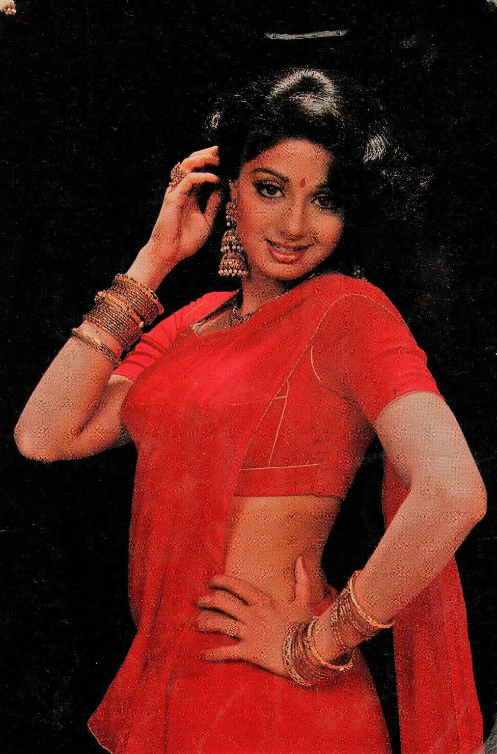 Sridevi 桌布 壁紙 — 一位身穿鮮紅色紗麗、佩戴金色珠寶的女性，在黑色背景前自信地擺姿勢。
