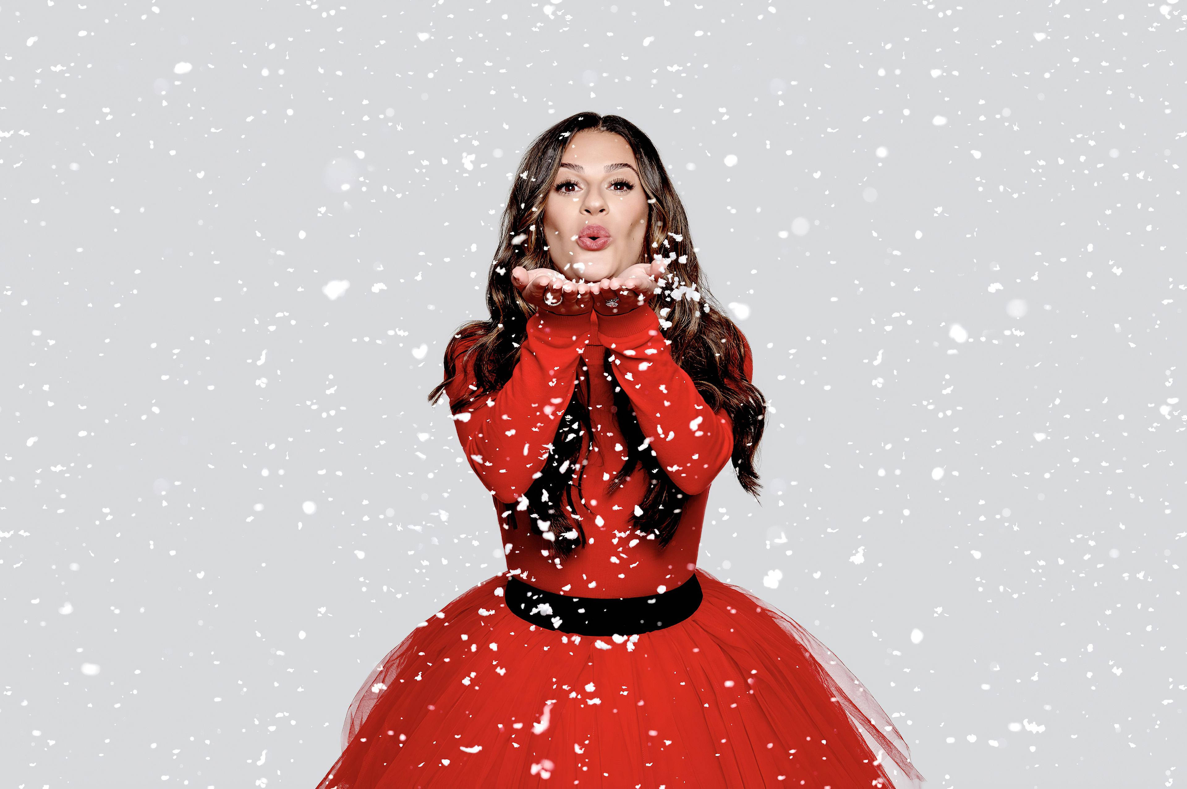 Lea Michele 桌布 壁紙 — 一位身穿鮮紅色連衣裙的女性，在白雪皚皚的灰色背景下，從她捧起的雙手中吹出雪花。