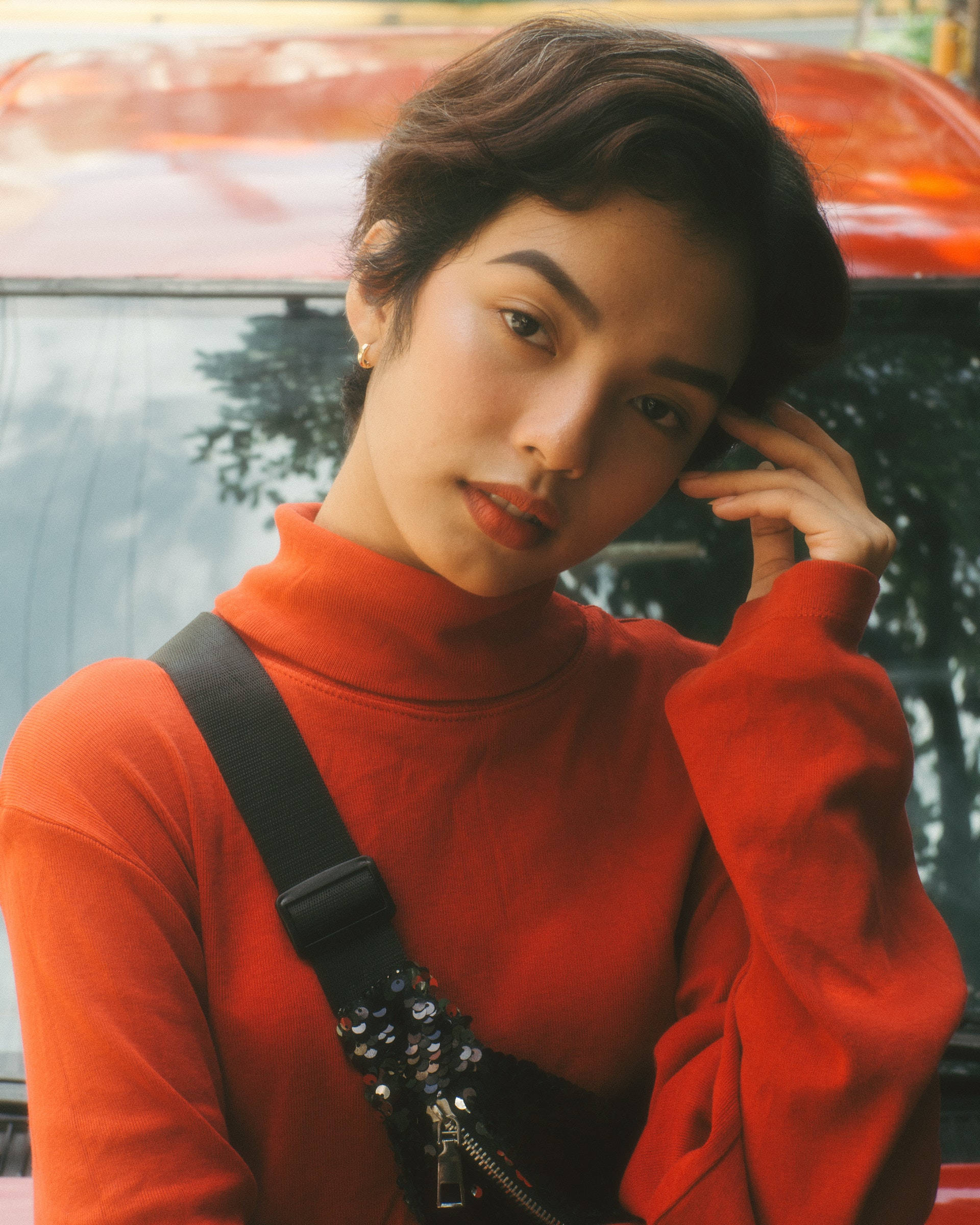 美女 桌布 壁紙 — 一位身穿鮮紅色高領毛衣的年輕女子，肩上掛著亮片手袋鏈條，若有所思地站在一輛紅色汽車旁。