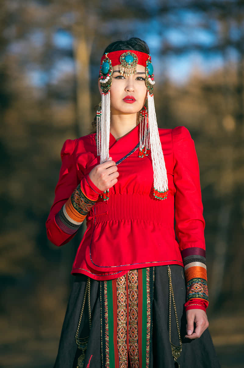 Woman 桌布 壁紙 — 一位身穿鮮豔傳統服飾的女性自信地站在陽光明媚的森林中，飾有精緻的珠飾和大膽的紅色點綴。