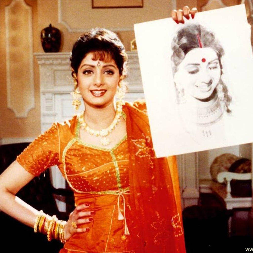 Sridevi 桌布 壁紙 — 一位身穿鮮豔橙色傳統服飾的女性微笑著舉起自己的肖像草圖。
