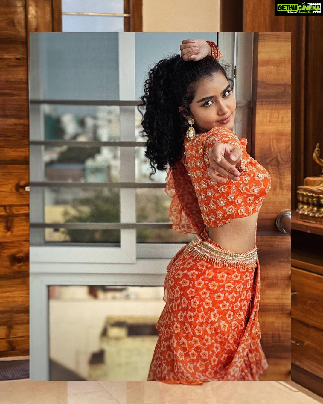 anupama parameswaran 桌布 壁紙 — 一位身穿鮮豔橙色圖案服裝的女性在室內自信地擺姿勢，以俏皮的笑容指向觀看者。