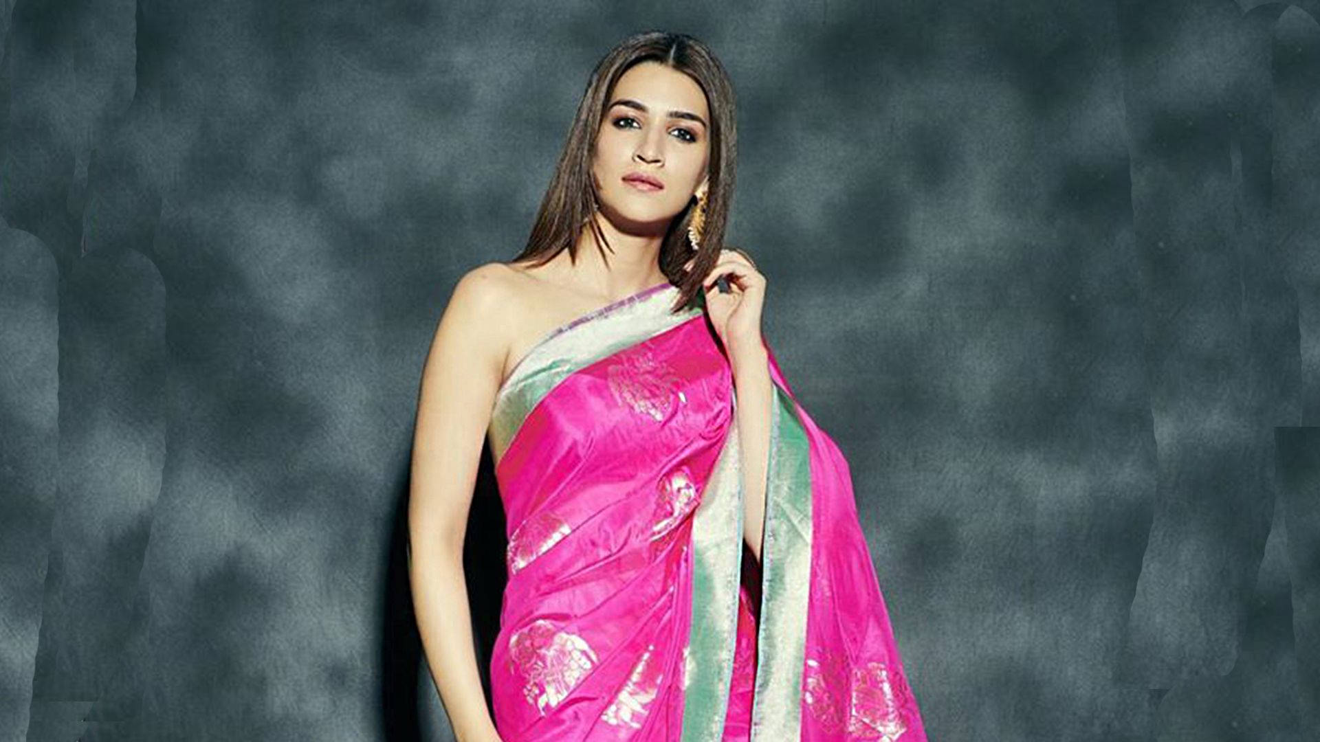 Kriti 桌布 壁紙 — 一位身穿鮮豔粉紅和綠色紗麗的女性，在帶有紋理的深灰色背景前自信地擺姿勢。