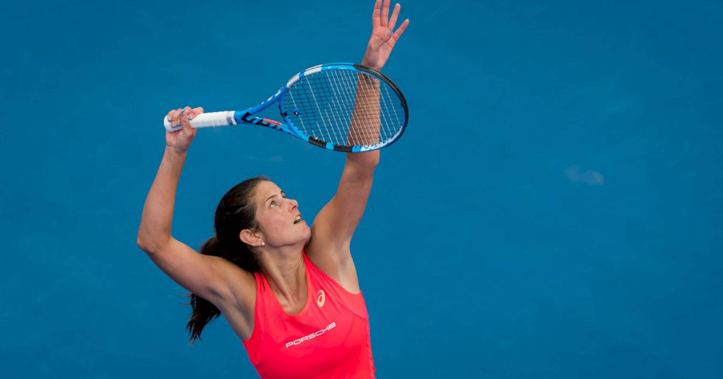 Tennis 桌布 壁紙 — 一位身穿鮮豔粉紅色上衣的女網球運動員，在純藍色球場背景下執行強力的過頭扣殺。