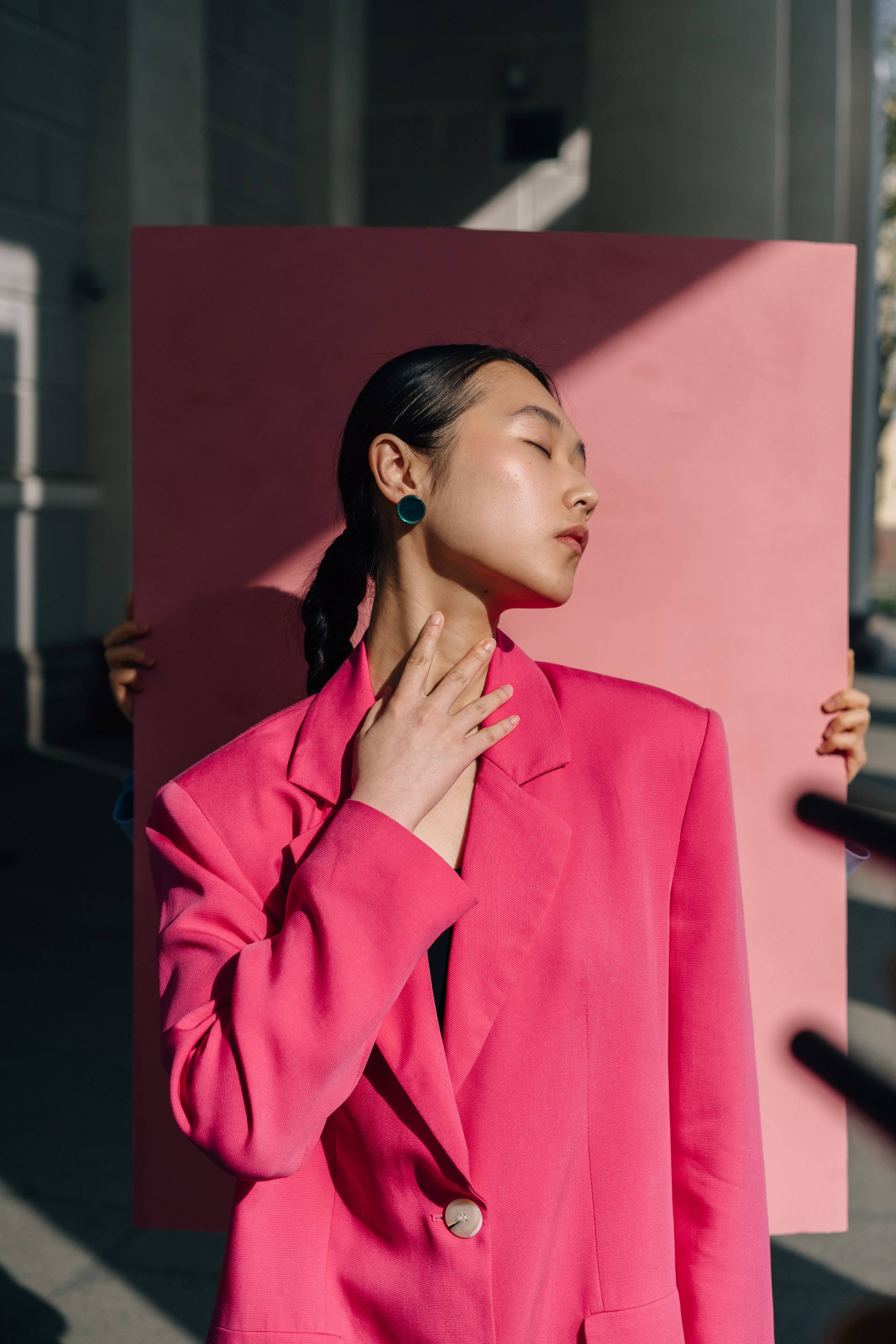 美女 桌布 壁紙 — 一位身穿鮮豔粉紅色西裝外套的女性，平靜地拿著一塊粉紅色板子，陽光在她的臉龐和周圍投下戲劇性的陰影。