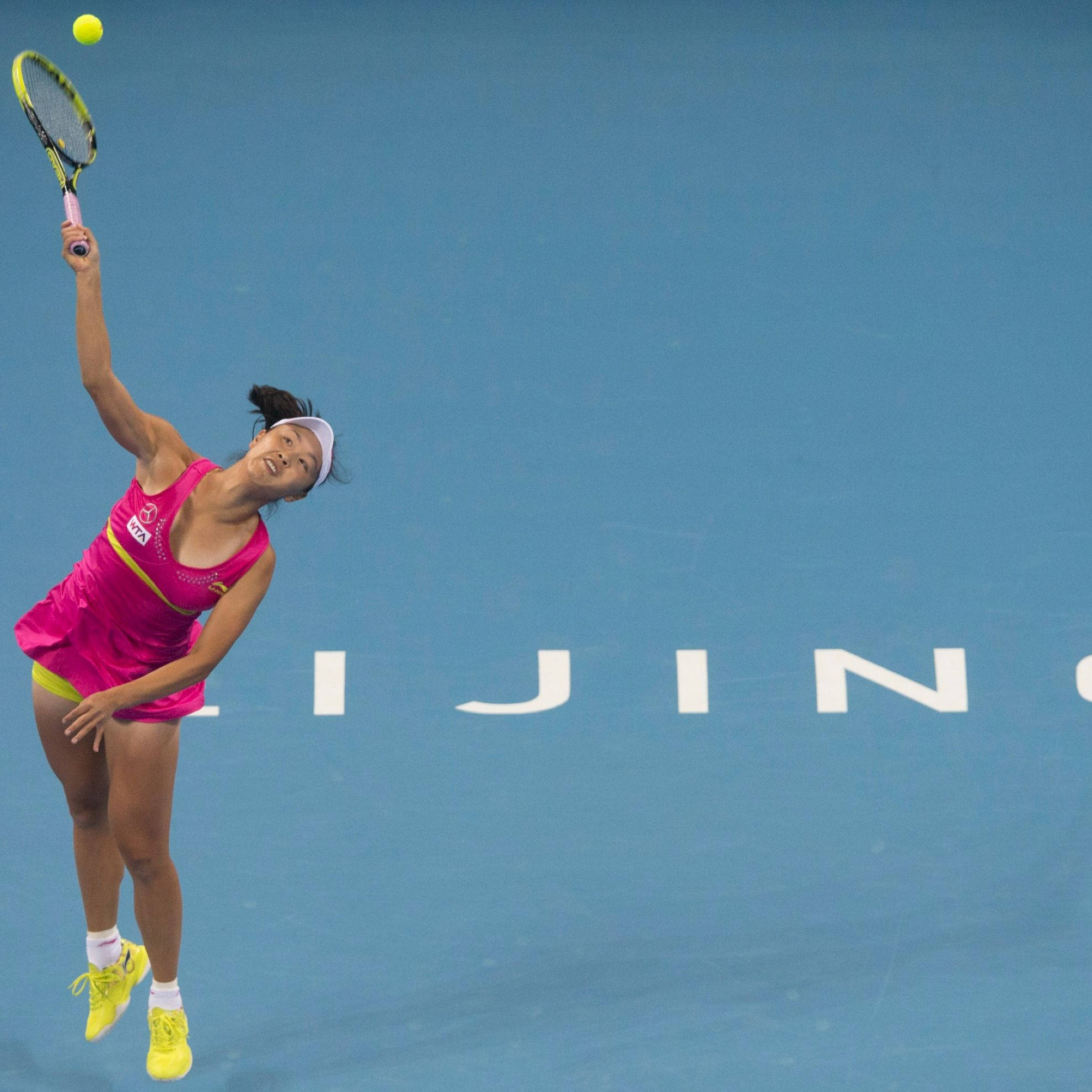 運動 桌布 壁紙 — 一位身穿鮮豔粉紅色運動服的女網球選手在藍色球場上跳起用球拍擊打黃色網球。
