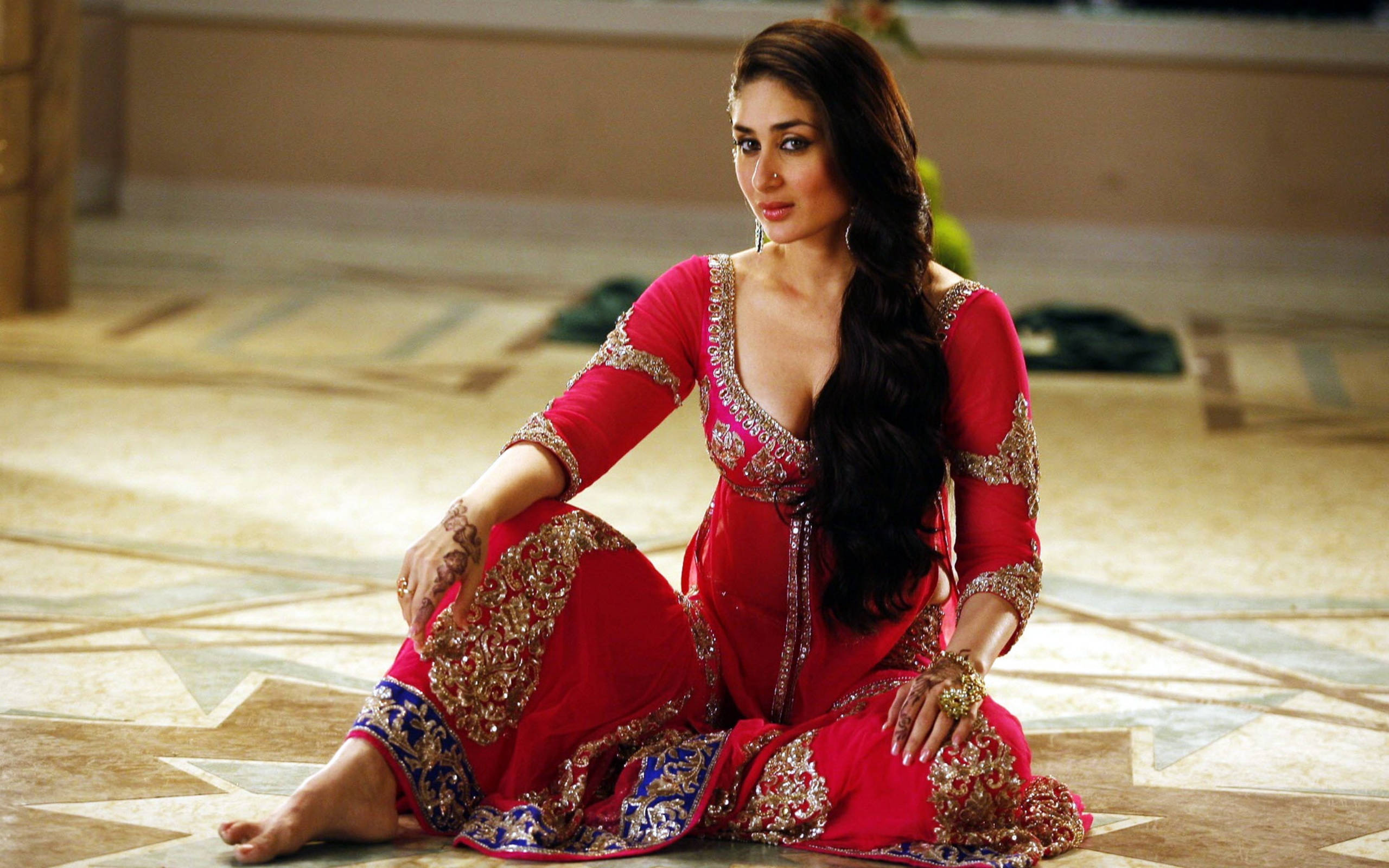 Kareena 桌布 壁紙 — 一位身穿鮮豔紅色刺繡紗麗的女性，雙手染有指甲花，長長的黑髮，優雅地坐在圖案地板上。